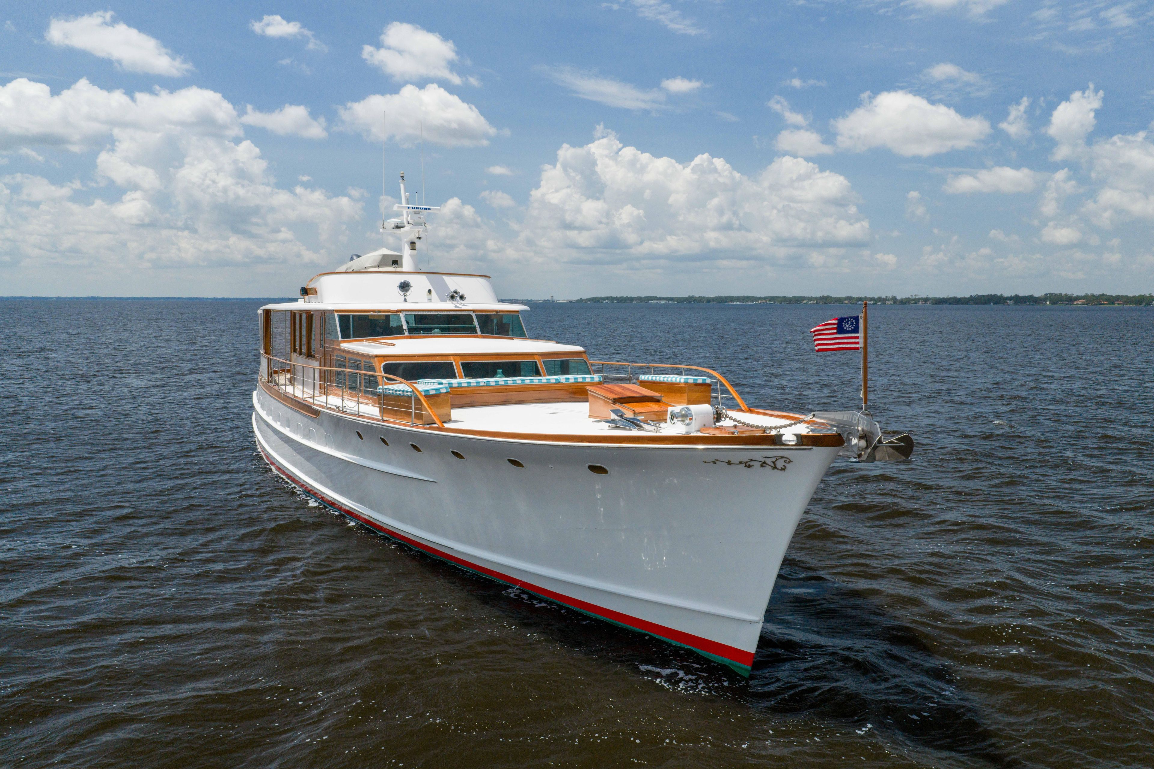 Classic 1963 Trumpy yacht on open water under a blue sky with clouds.