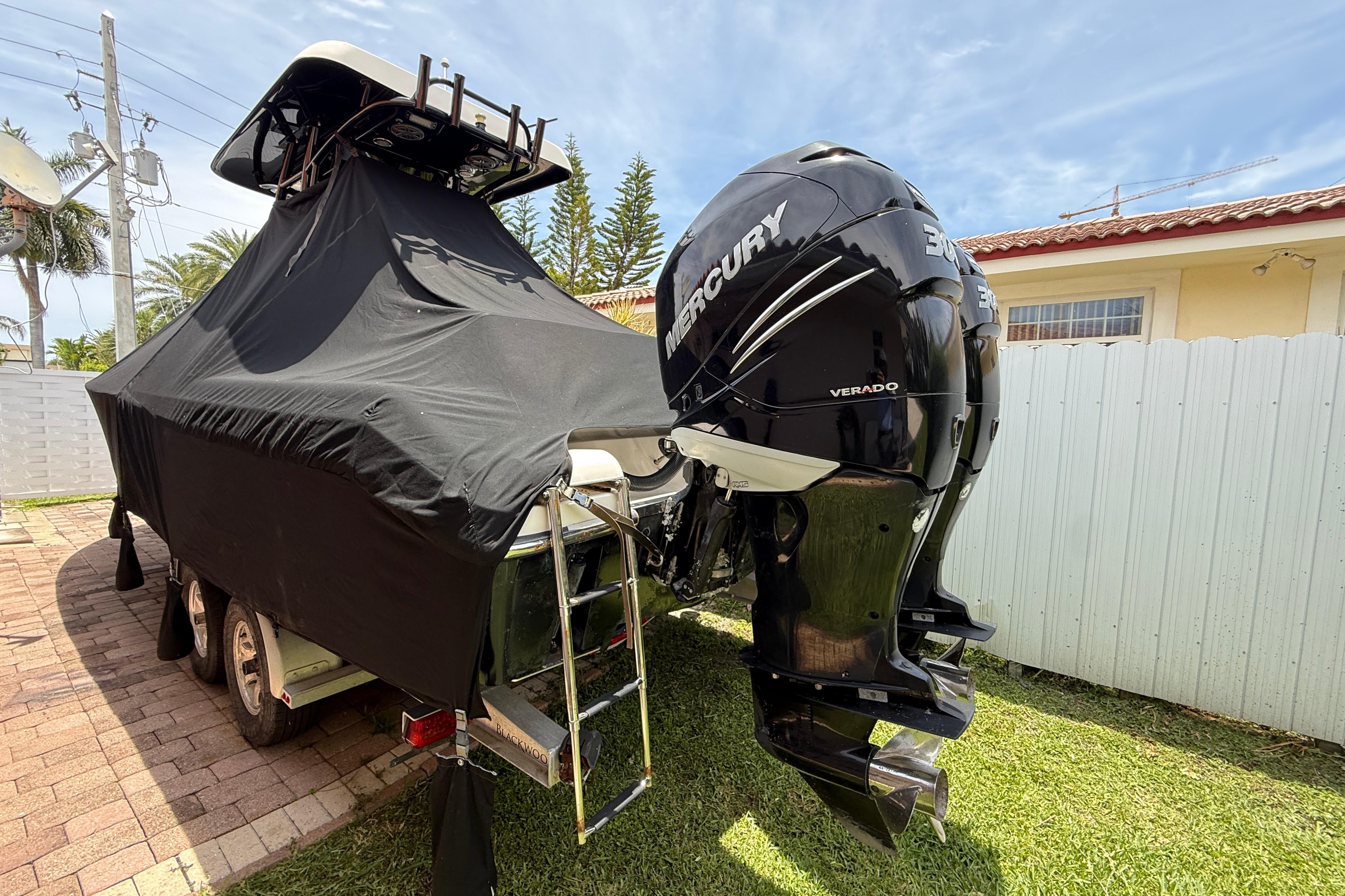 Covered Blackwood 27 boat with Mercury Verado engine, parked on a brick driveway.