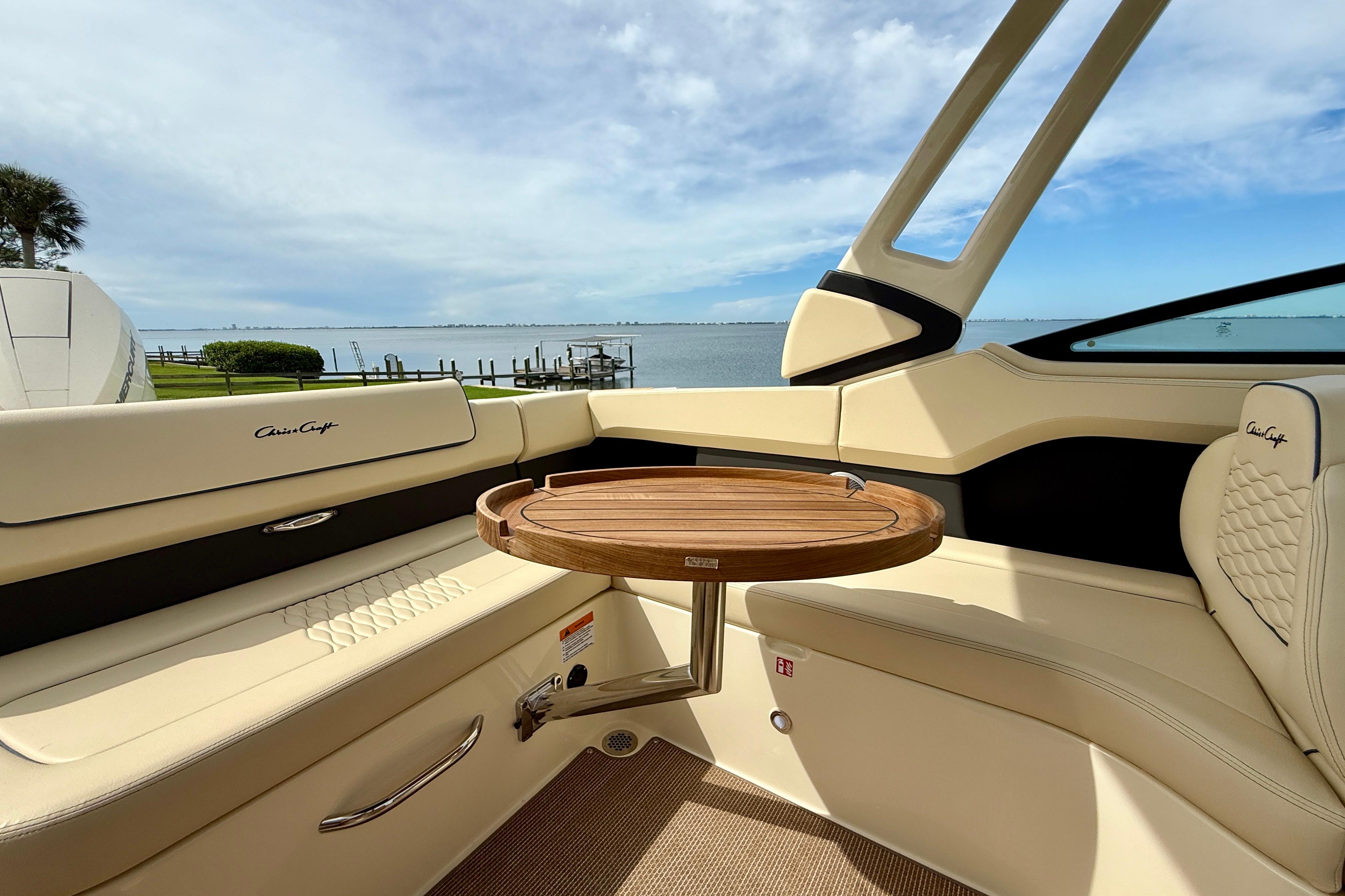 2026 Chris-Craft Sportster 28 interior with elegant seating and wooden table, overlooking serene waters.