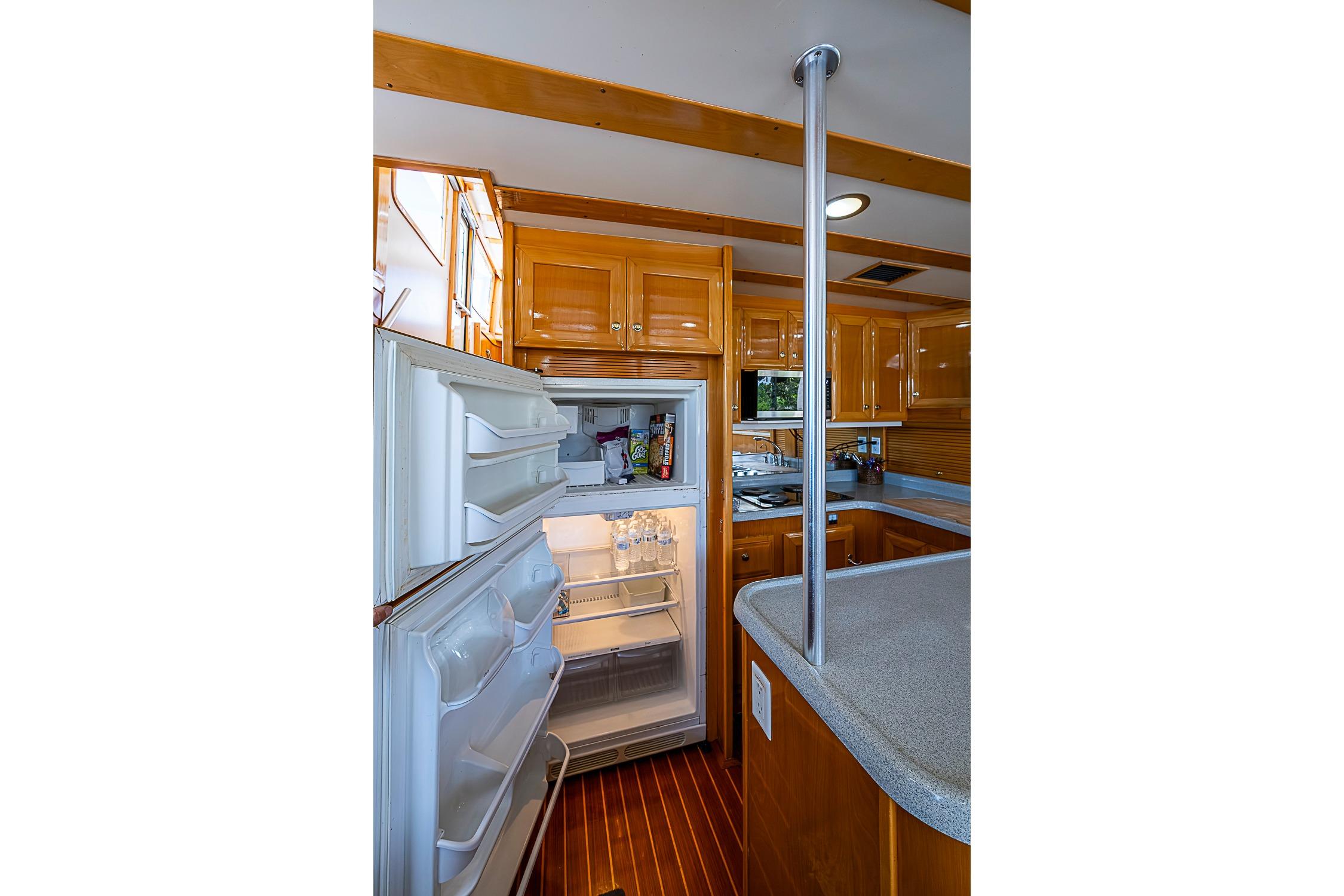 Galley kitchen in 2003 Magna Marine Nova Scotia 47 yacht with open fridge and wooden cabinetry.
