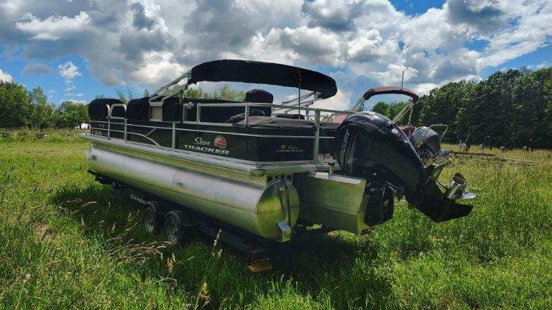 A 2019 White River SF22XP3 PB BK pontoon boat on a trailer in a grassy field.