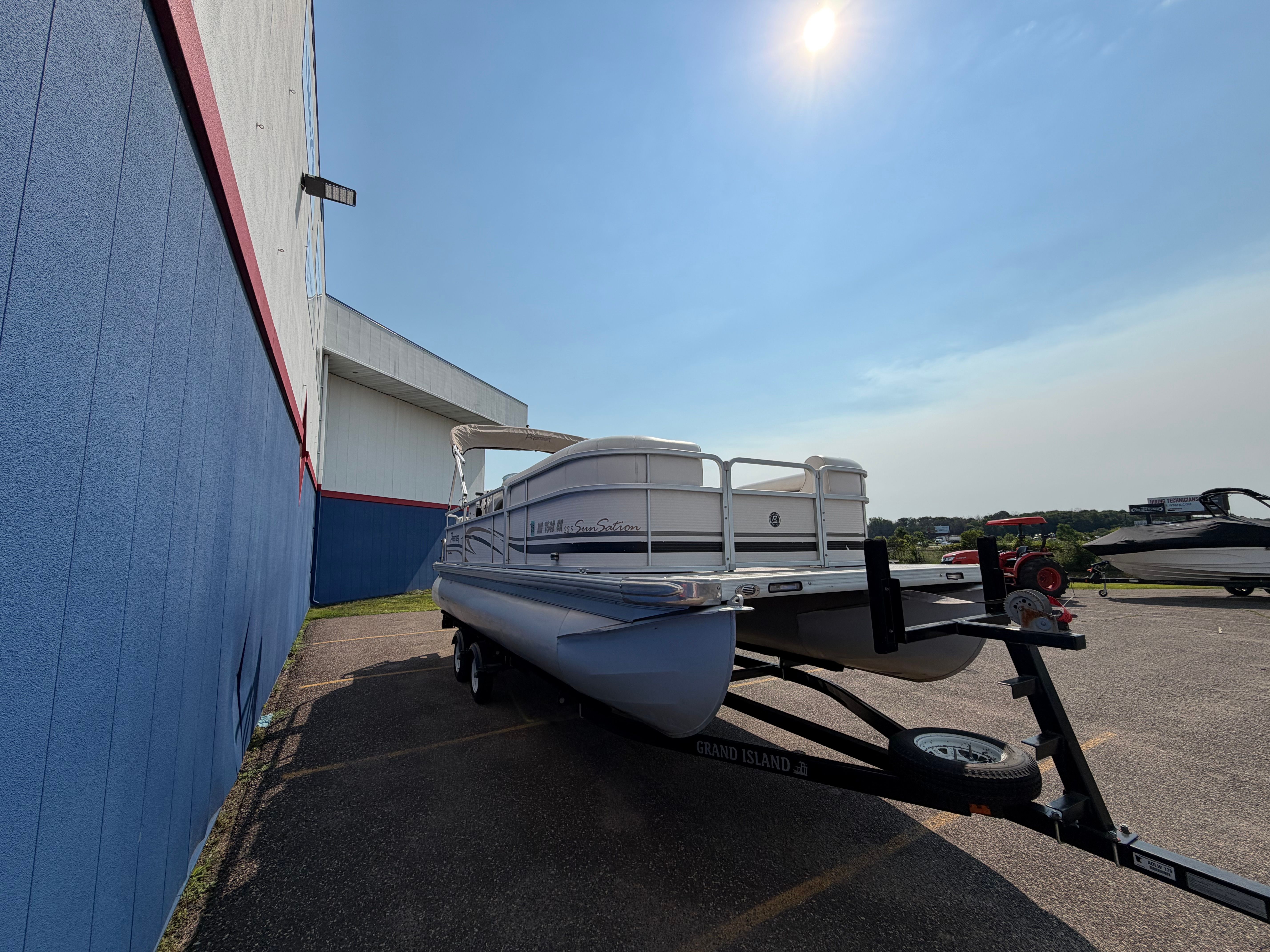Premier 225 Sunsation pontoon boat from 2007 on a trailer next to a building.