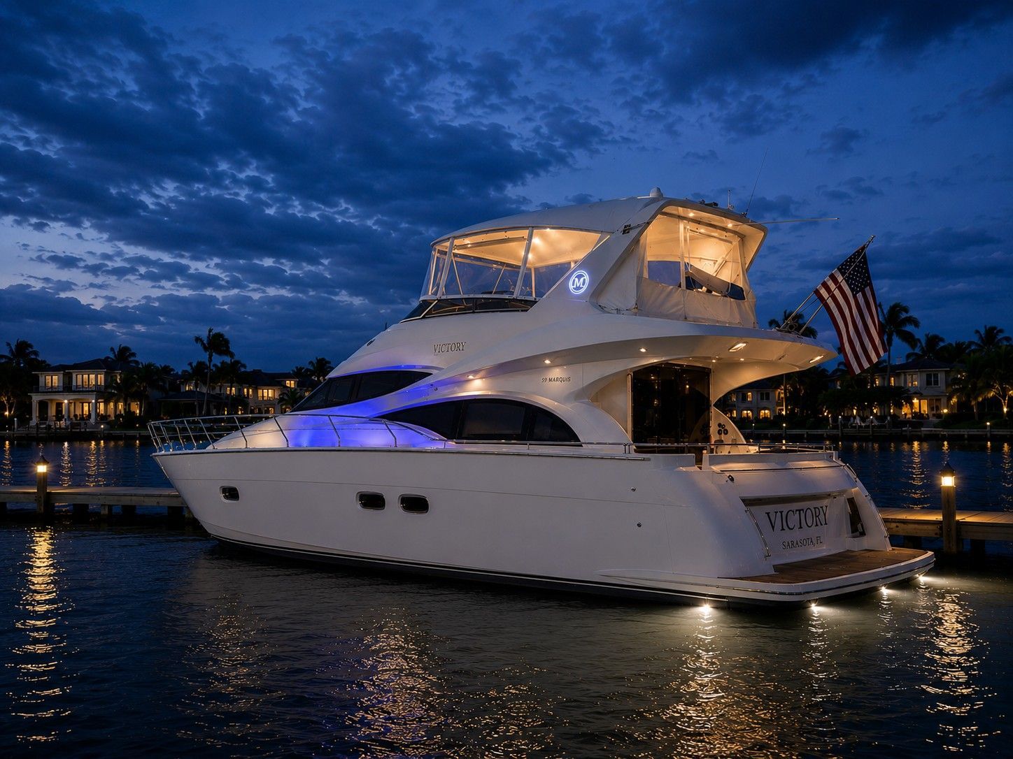 A luxurious yacht is docked at night, illuminated by blue lights, with an American flag.