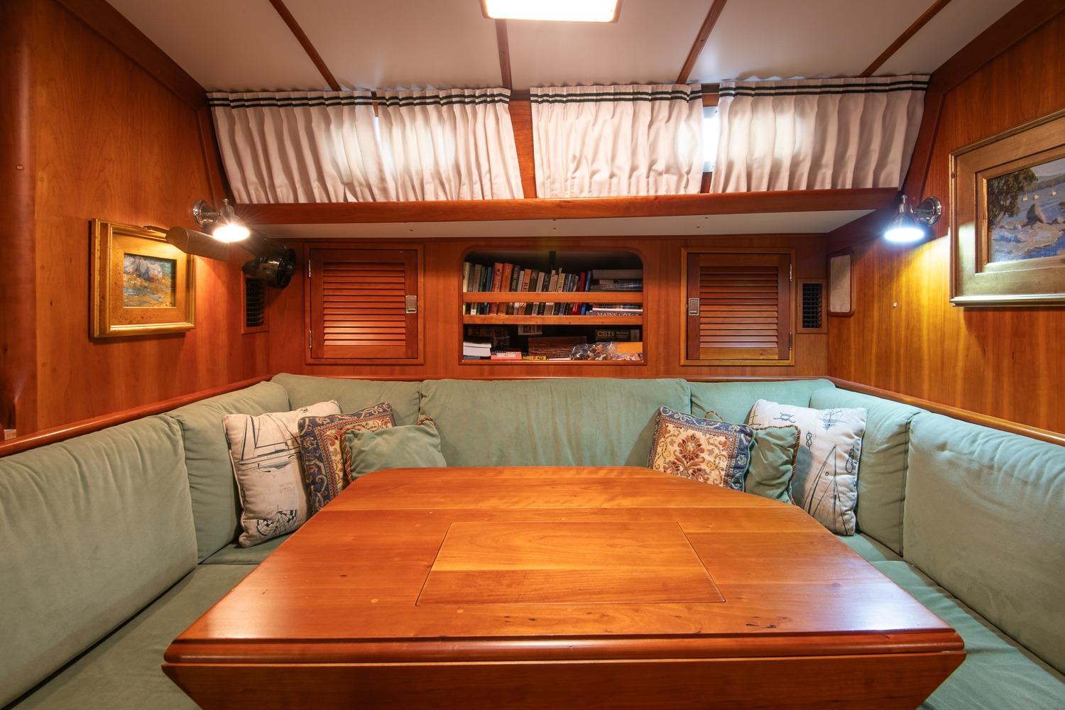 Cozy interior of 1989 Hinckley Sou'wester 51 yacht with wooden table and cushioned seating.