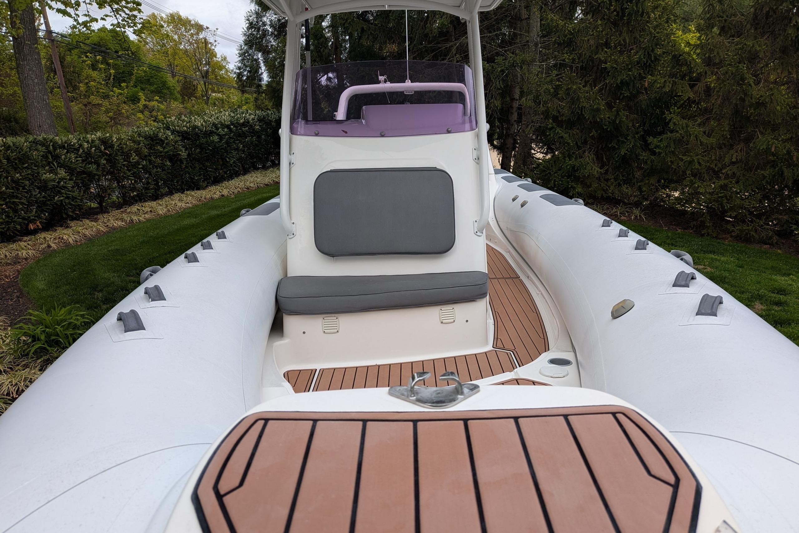 2016 Brig E780 inflatable boat with cushioned seating and wooden deck, surrounded by greenery.