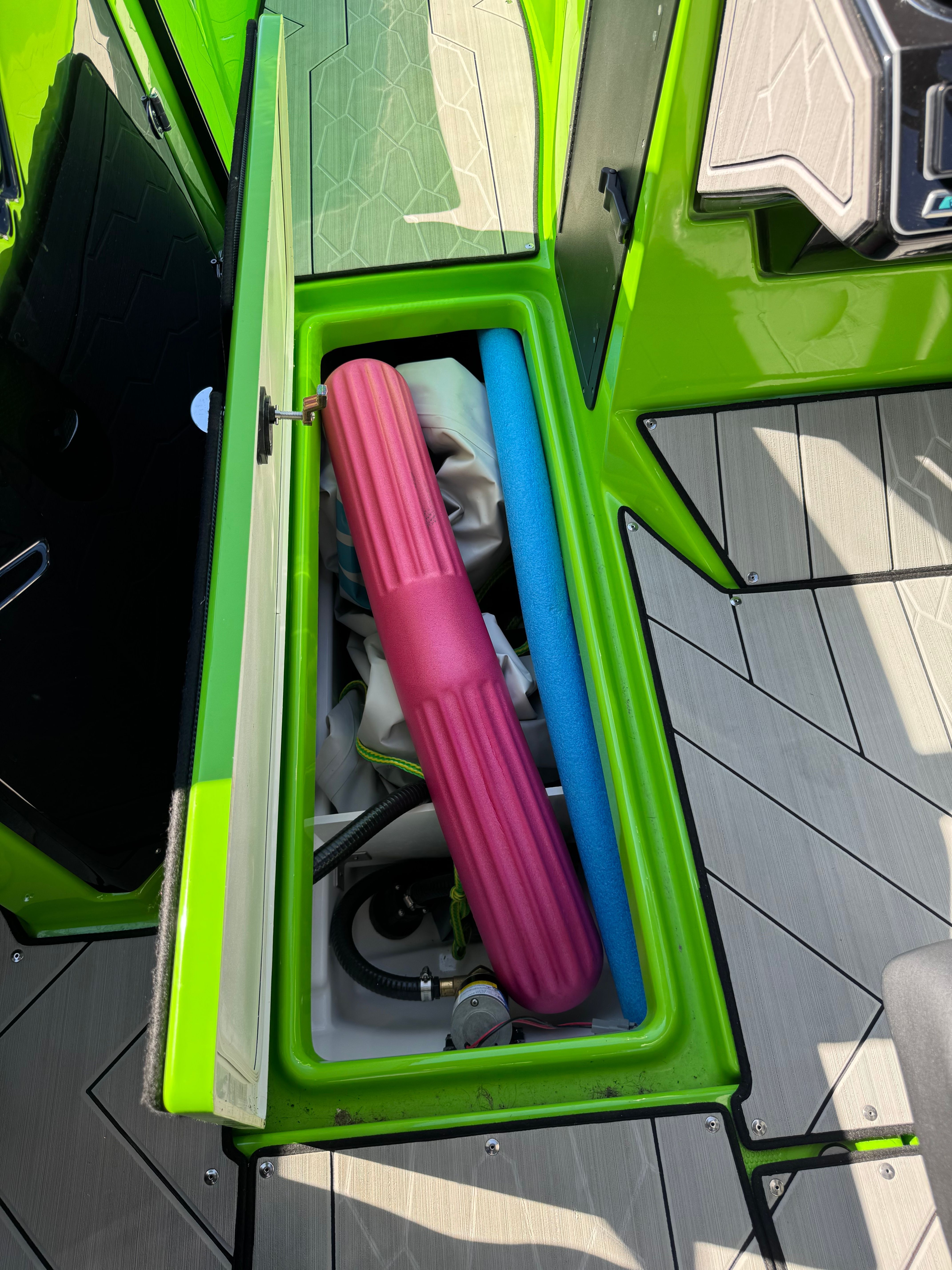 A green storage compartment on a Yamaha 255XD boat with pool noodles and accessories.