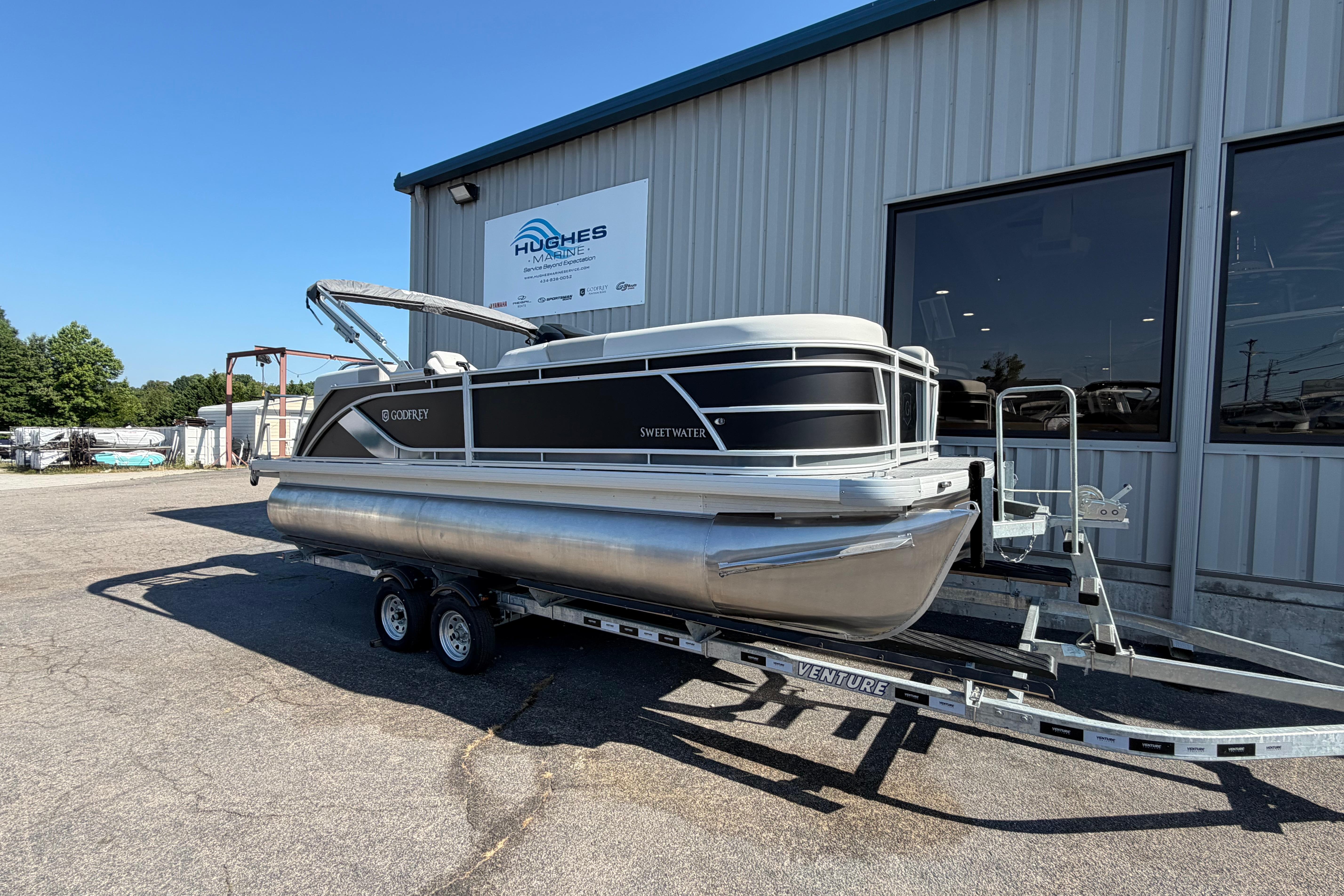 2026 Godfrey Sweetwater 2086 SBC pontoon boat on trailer outside Hughes Marine building.