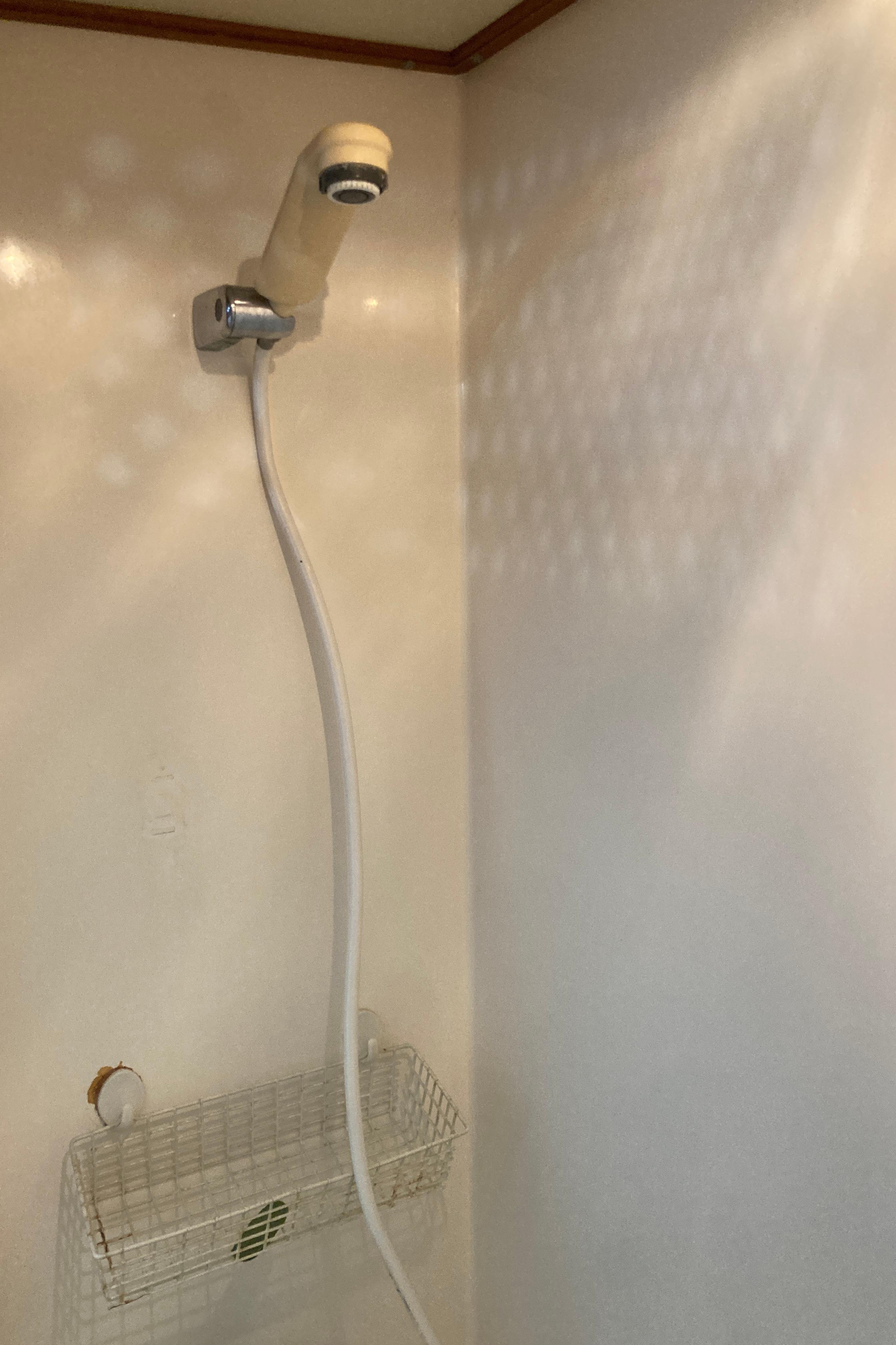Shower area in 1991 Trader 47 boat with wall-mounted showerhead and wire basket.