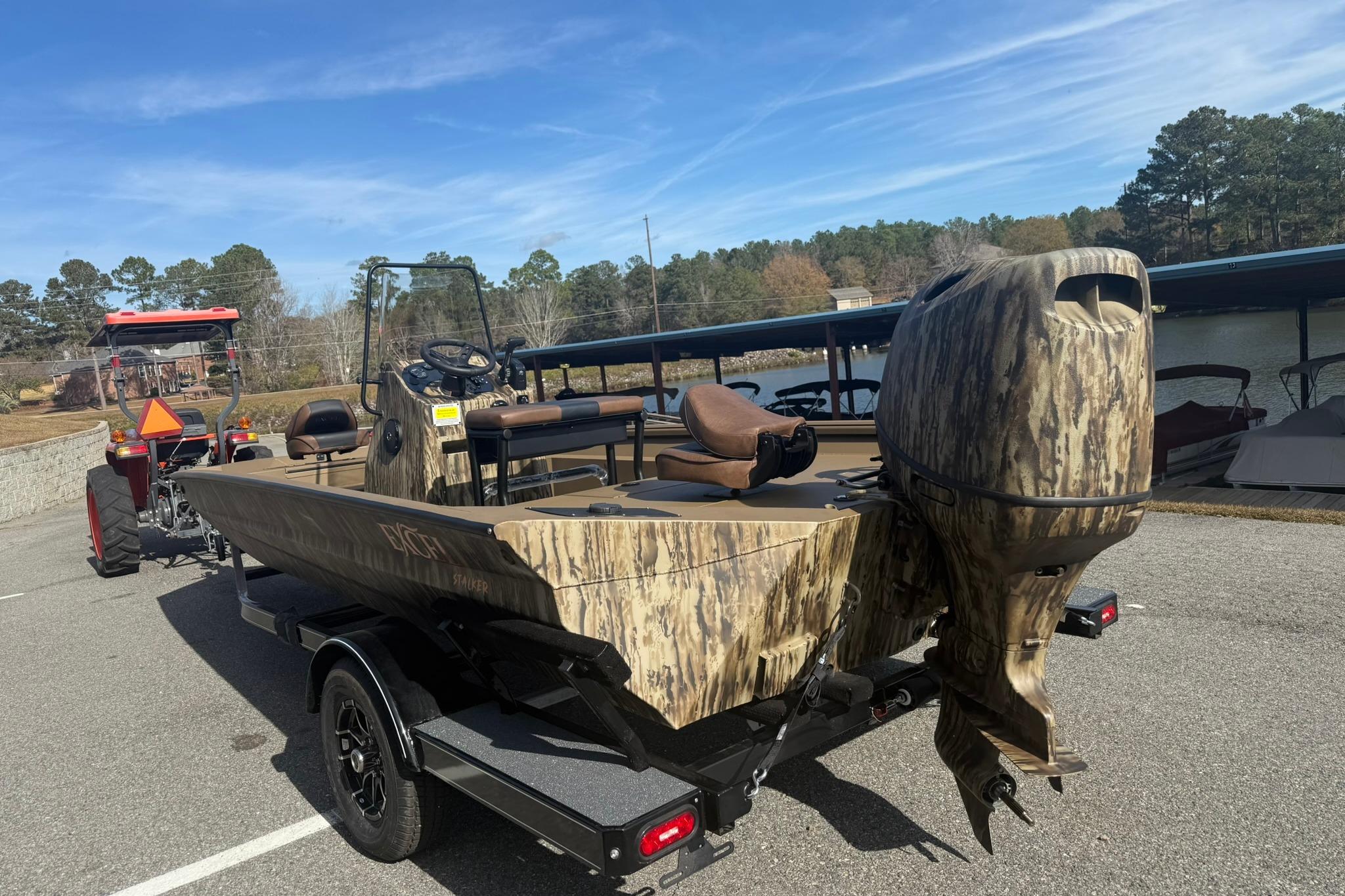 Camouflage-patterned 2026 Excel 206 Stalker CC boat on trailer, parked near a lake.