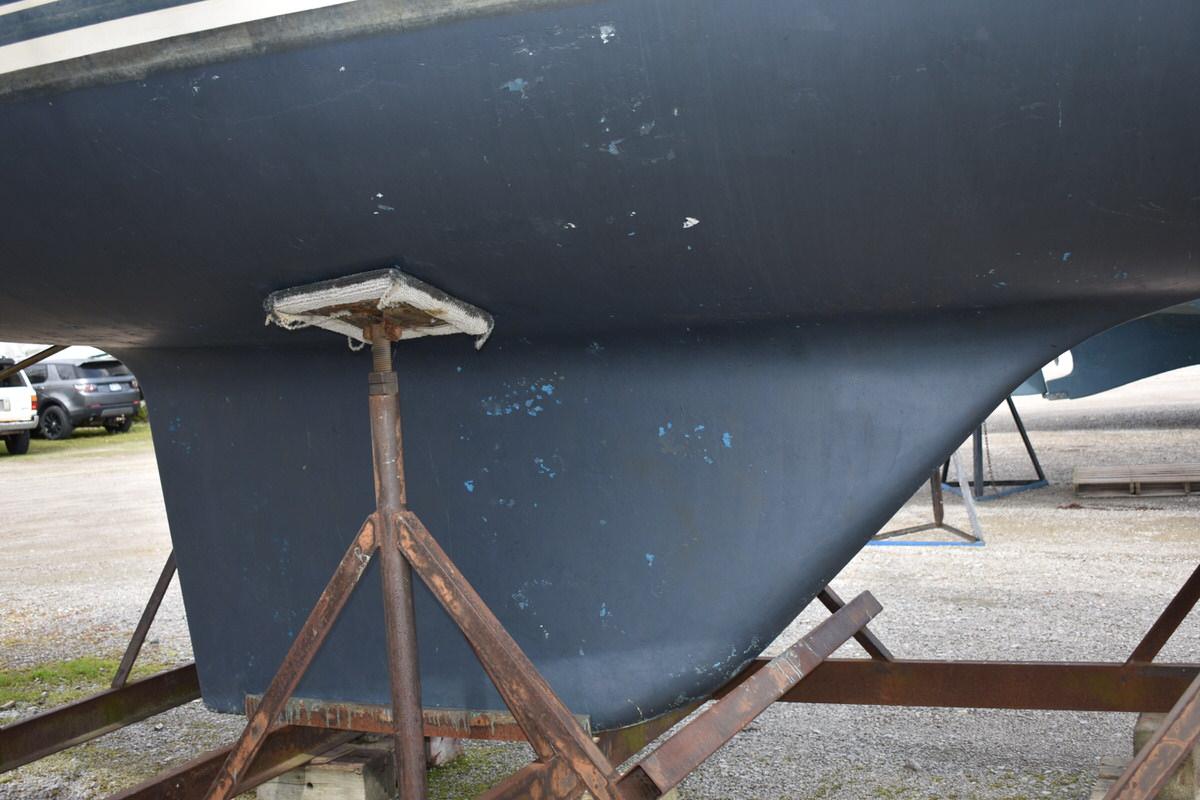 The hull of a blue sailboat on a stand, showing some wear marks.