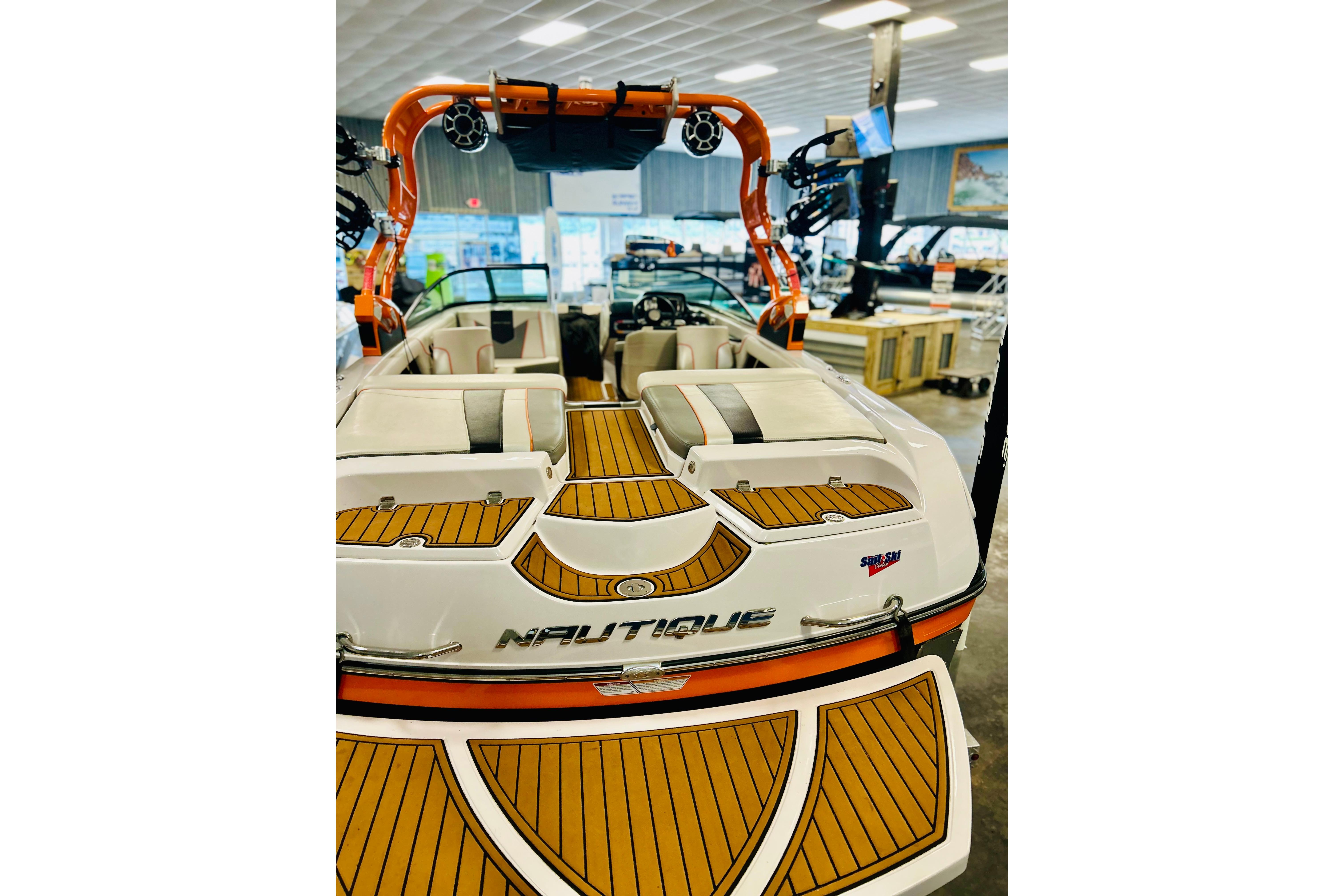 2013 Nautique Super Air Nautique 230 boat with teak deck and orange accents in showroom.