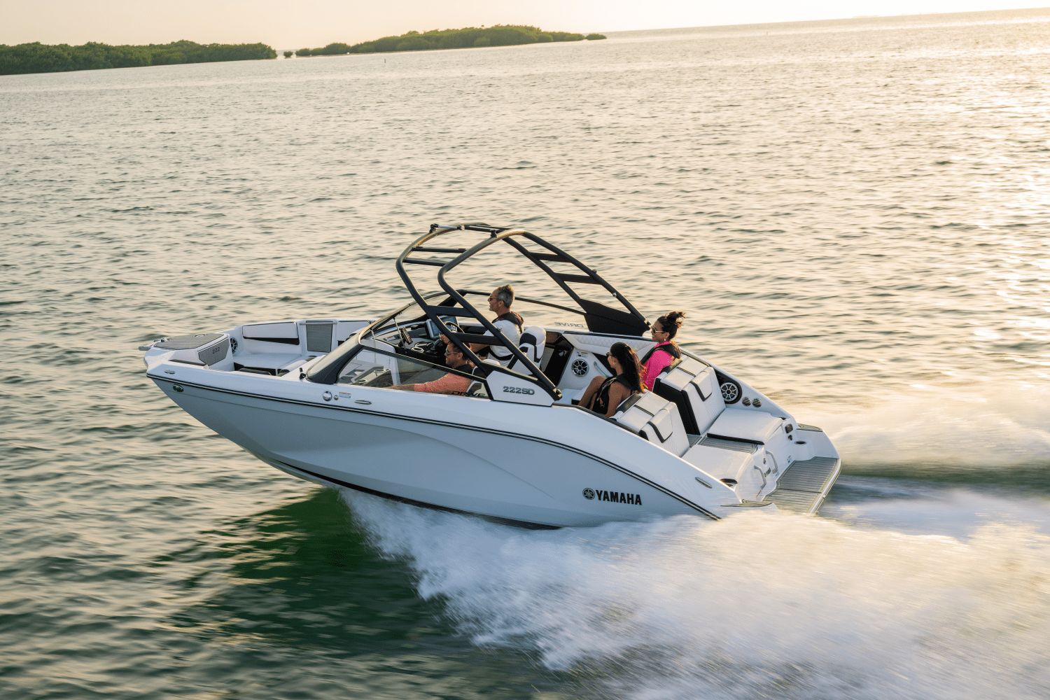 A modern Yamaha boat speeds across the water at sunset.