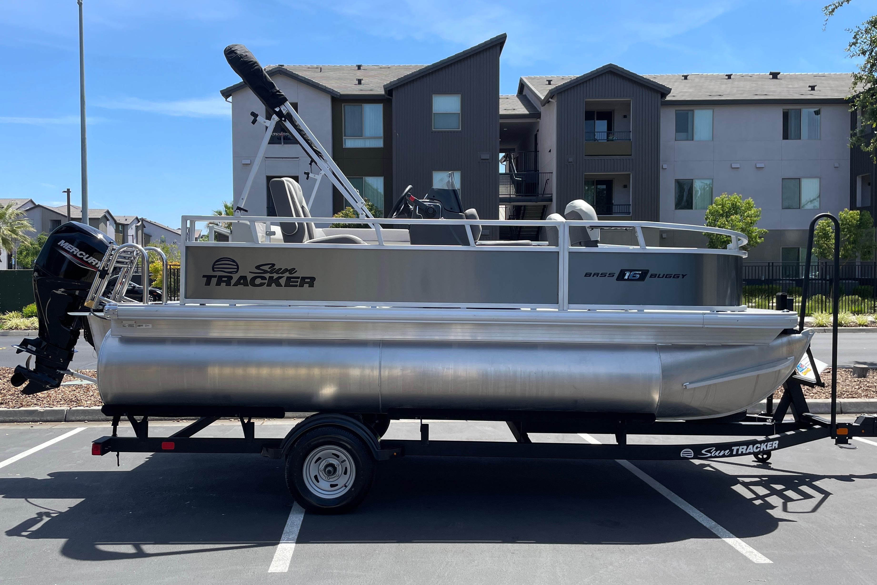 2026 Sun Tracker Bass Buggy 16 XL Select pontoon boat on trailer in parking lot.