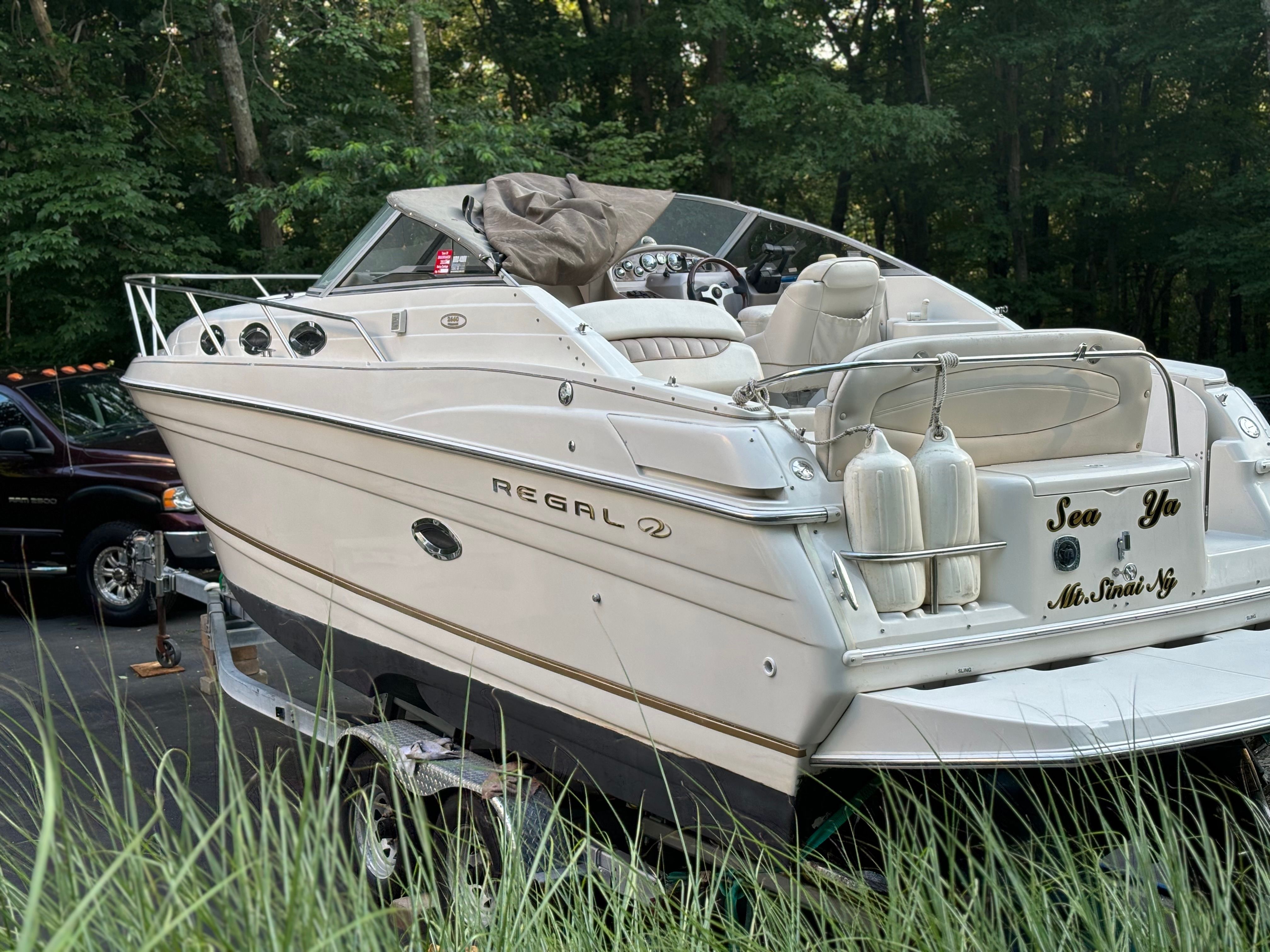 A Regal Commodore 2660 boat on a trailer, surrounded by trees.