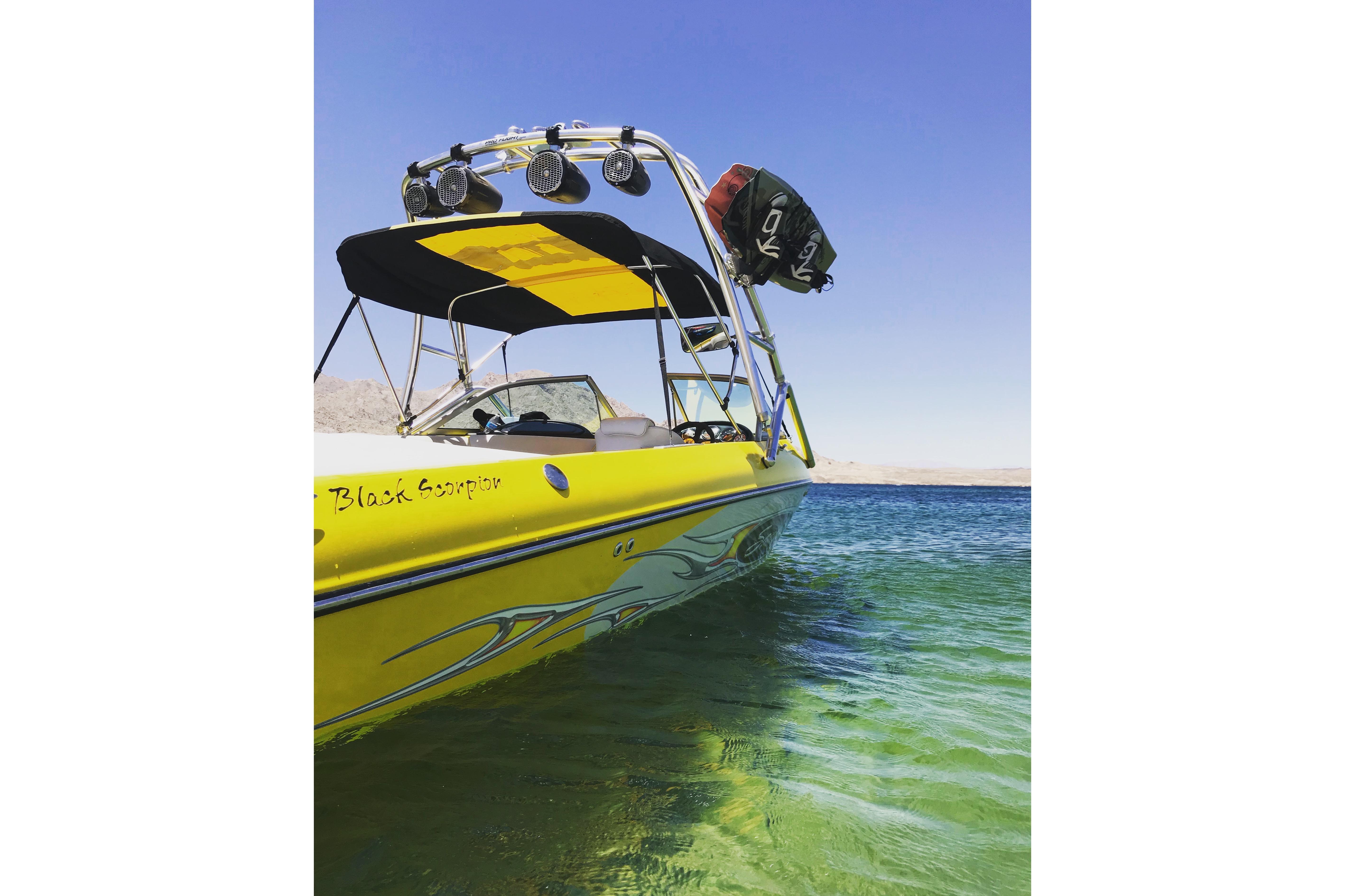 Yellow 2006 Sanger V230 boat on clear water with blue sky background.