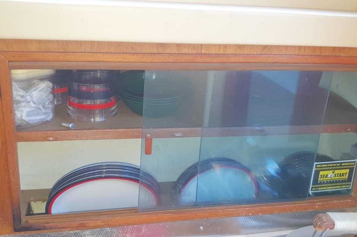Wooden cabinet with glass doors on a 1989 Fairey Spearfish MKIII, storing dishes and containers.