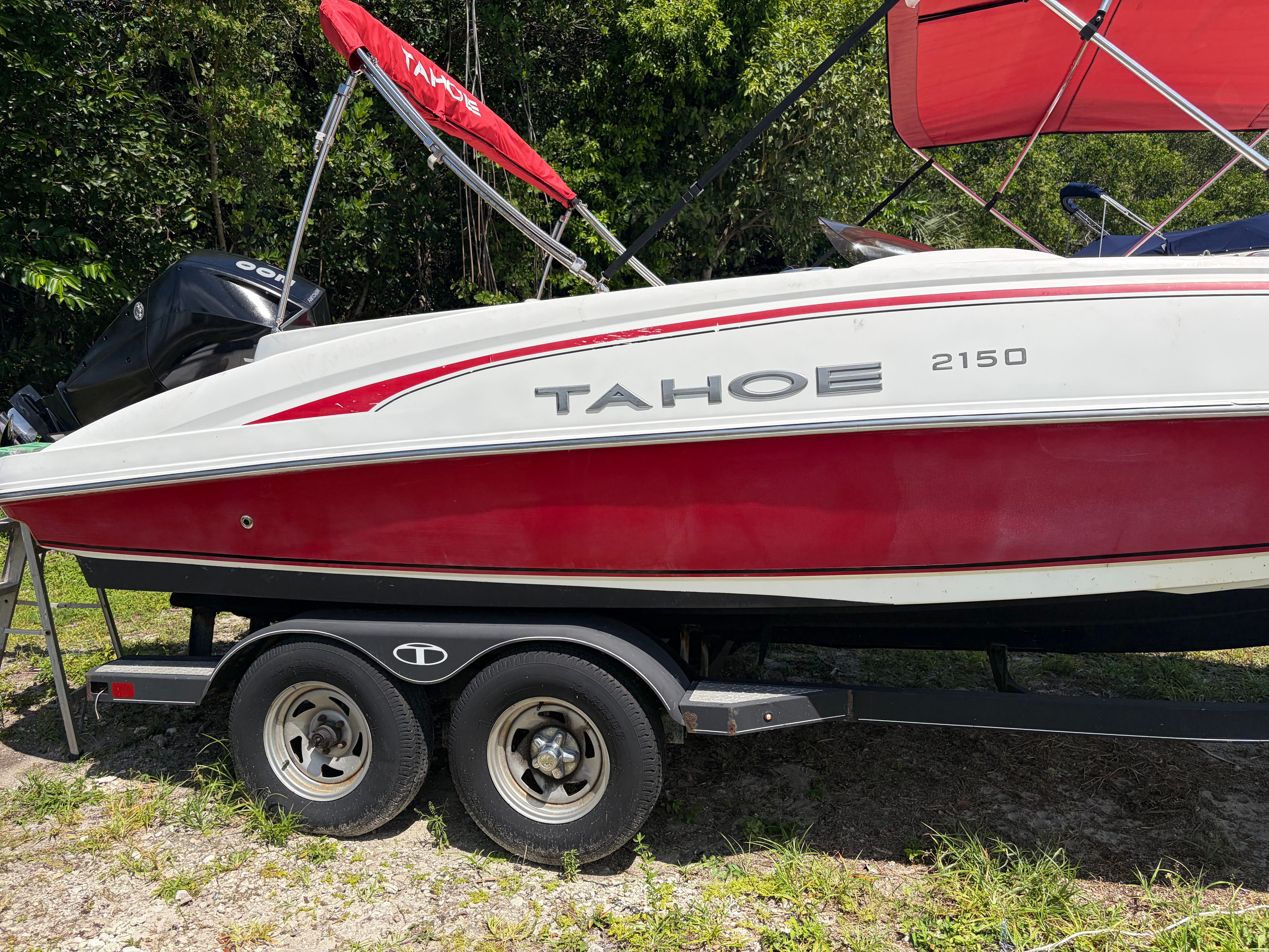 A red Tahoe 2150 boat on a trailer, surrounded by trees.