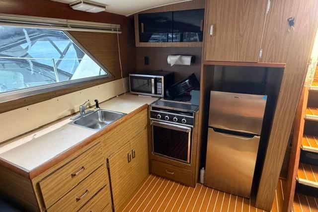 1980 Chris-Craft 381 Catalina yacht kitchen with wood cabinetry, stove, microwave, and refrigerator.
