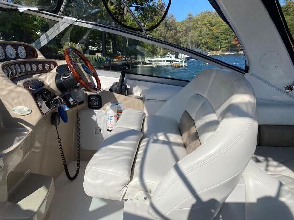 Interior of a boat with beige cockpit and white seat, surrounded by water and trees.