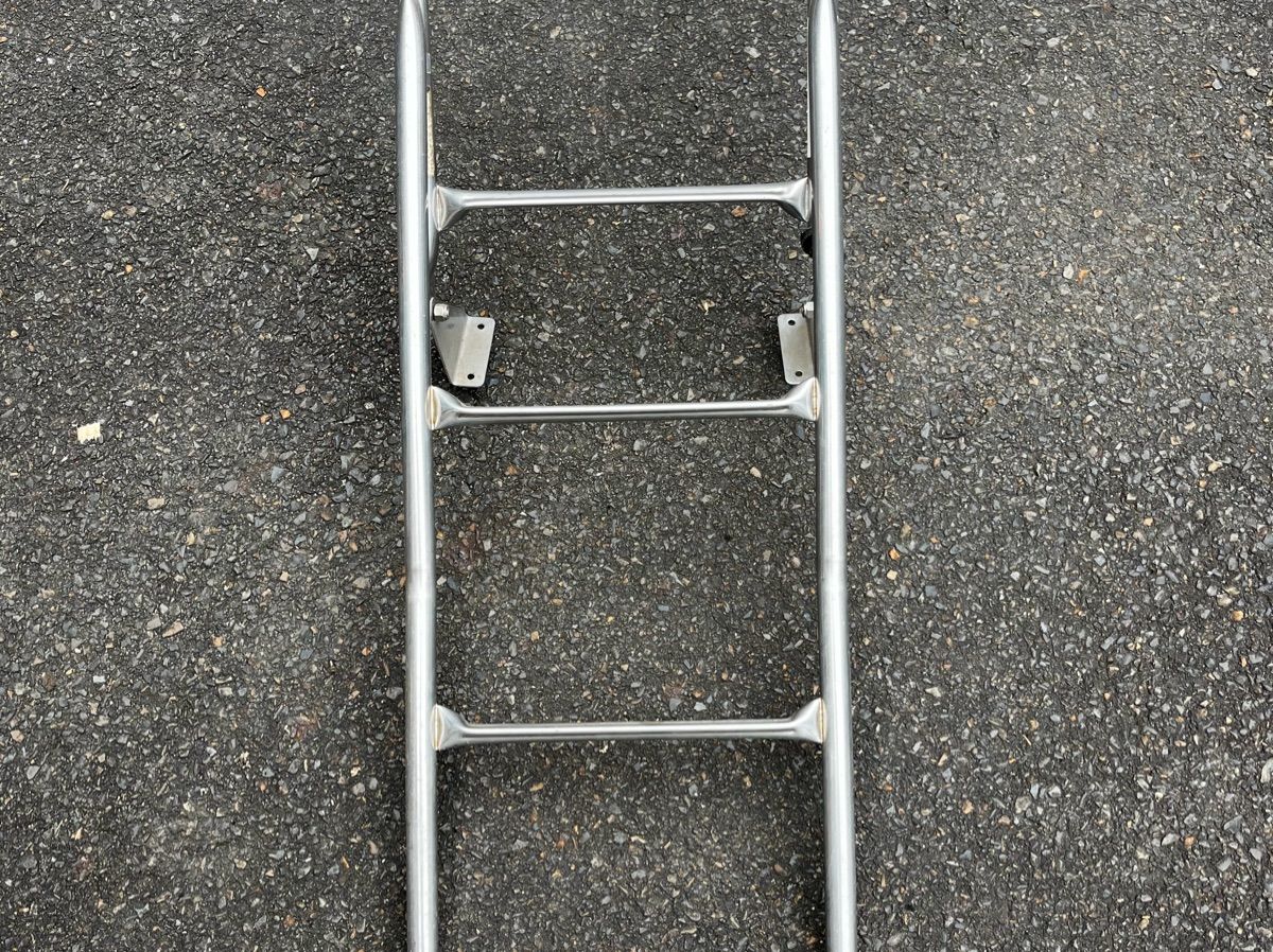A silver metal ladder lies on an asphalt surface.