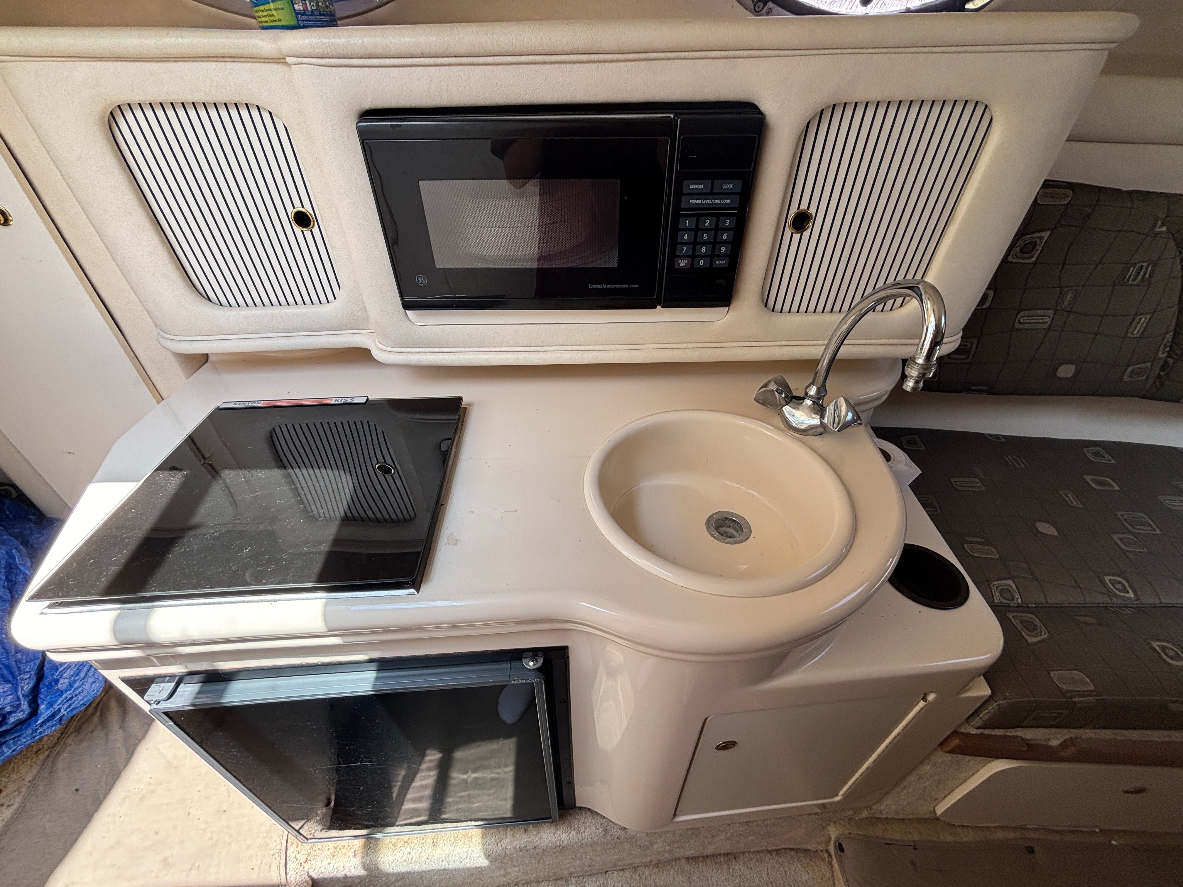 Compact kitchenette with sink, stove, microwave, and fridge inside a boat.