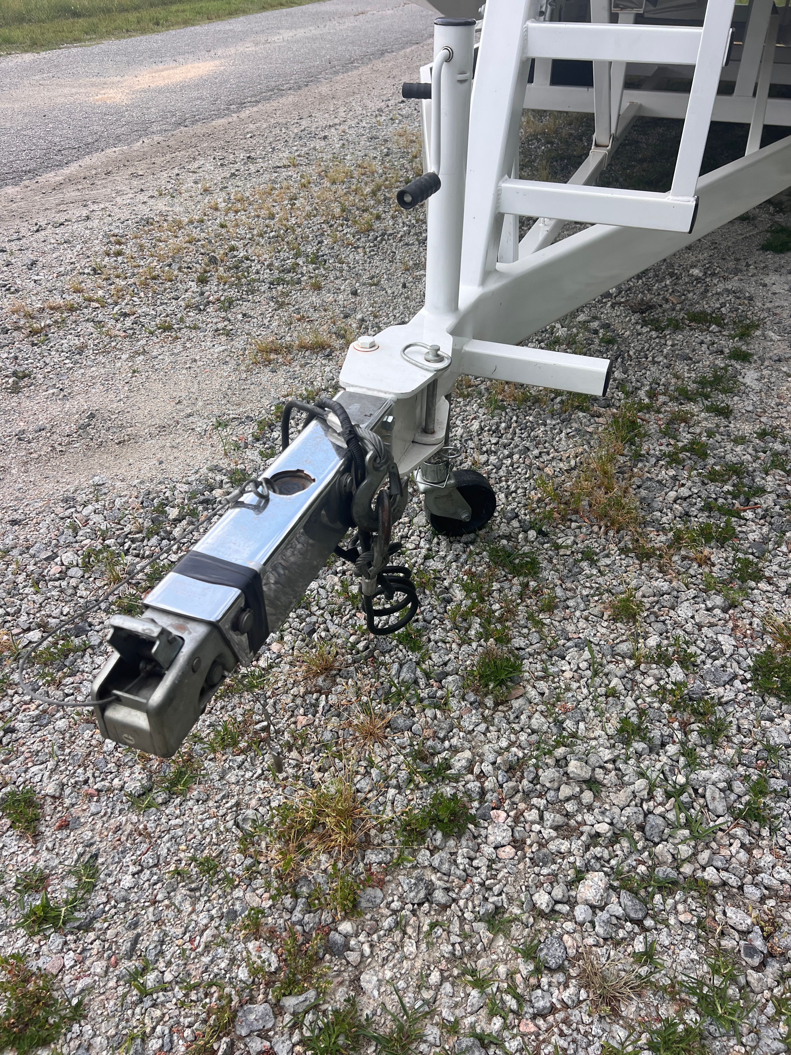 Close-up of a boat trailer on a gravel path, featuring a sturdy metal frame.