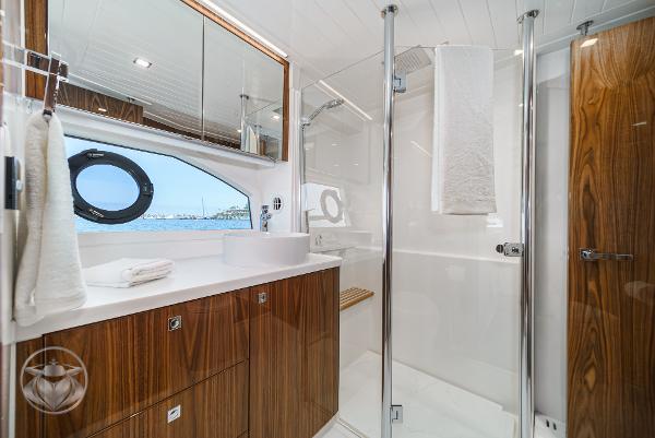 Luxurious bathroom in the 2025 Riviera 645 SUV yacht with wooden cabinetry and glass shower.