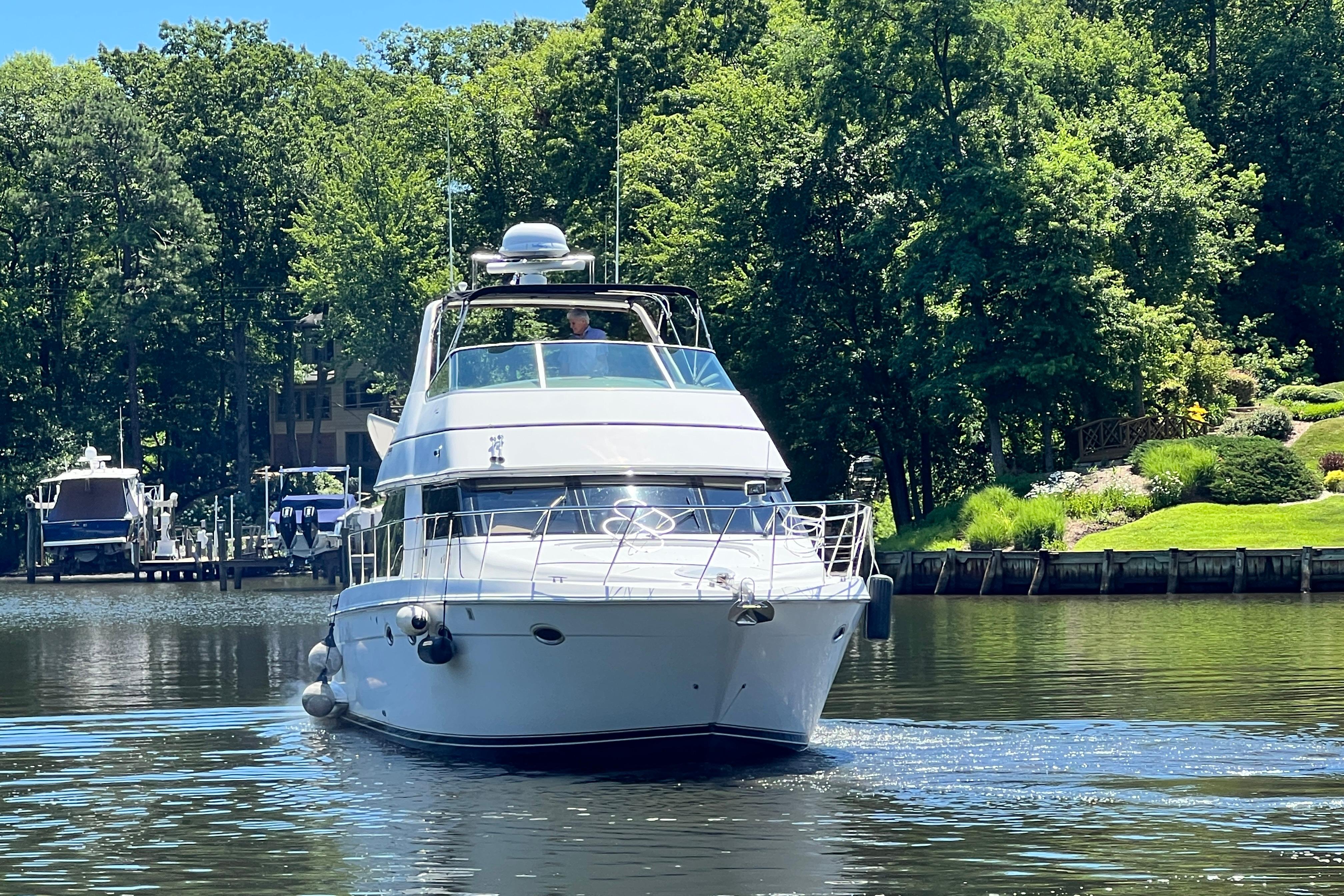 2003 Carver 450 Voyager Pilothouse yacht cruising on a serene lake with lush greenery.