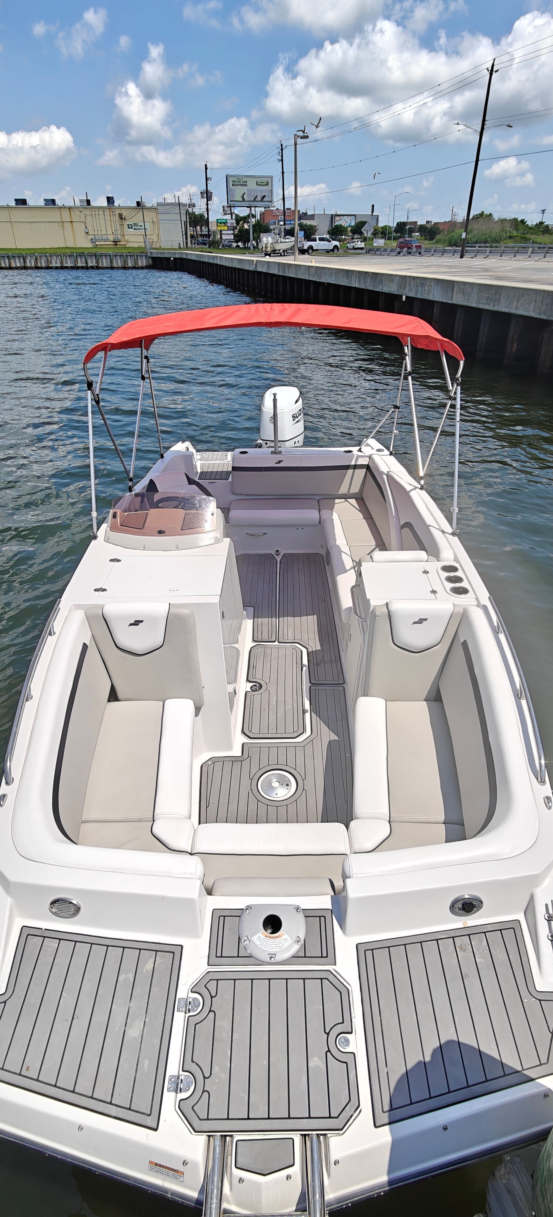 A Starcraft SVX 231 boat with a red canopy on calm water near a shoreline.