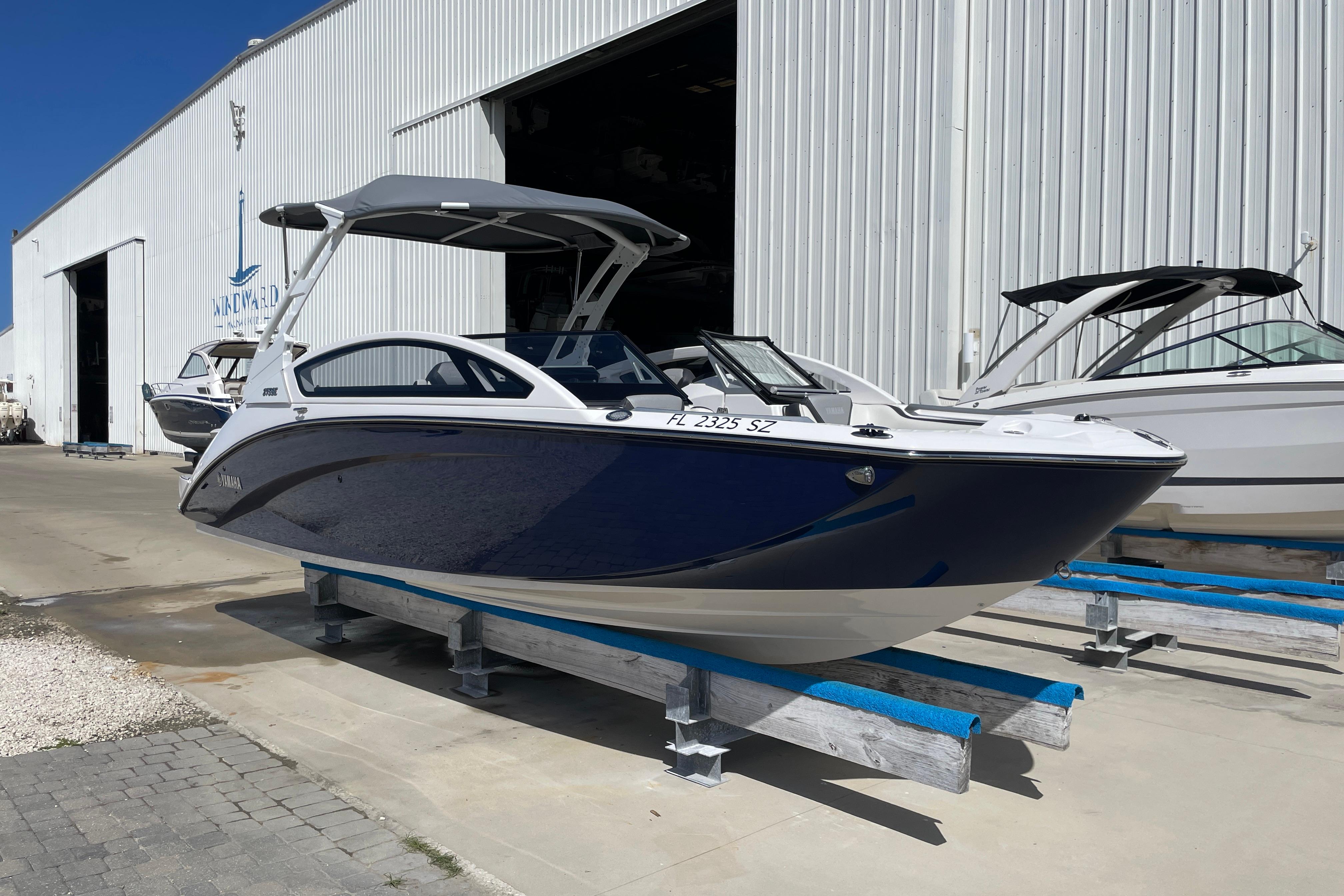 2021 Yamaha Boats 275SE in marina, blue and white, docked outside a large warehouse.