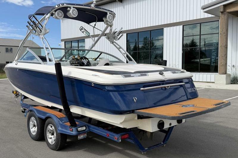 2004 MasterCraft XStar boat on trailer, blue and white, parked outside a building.