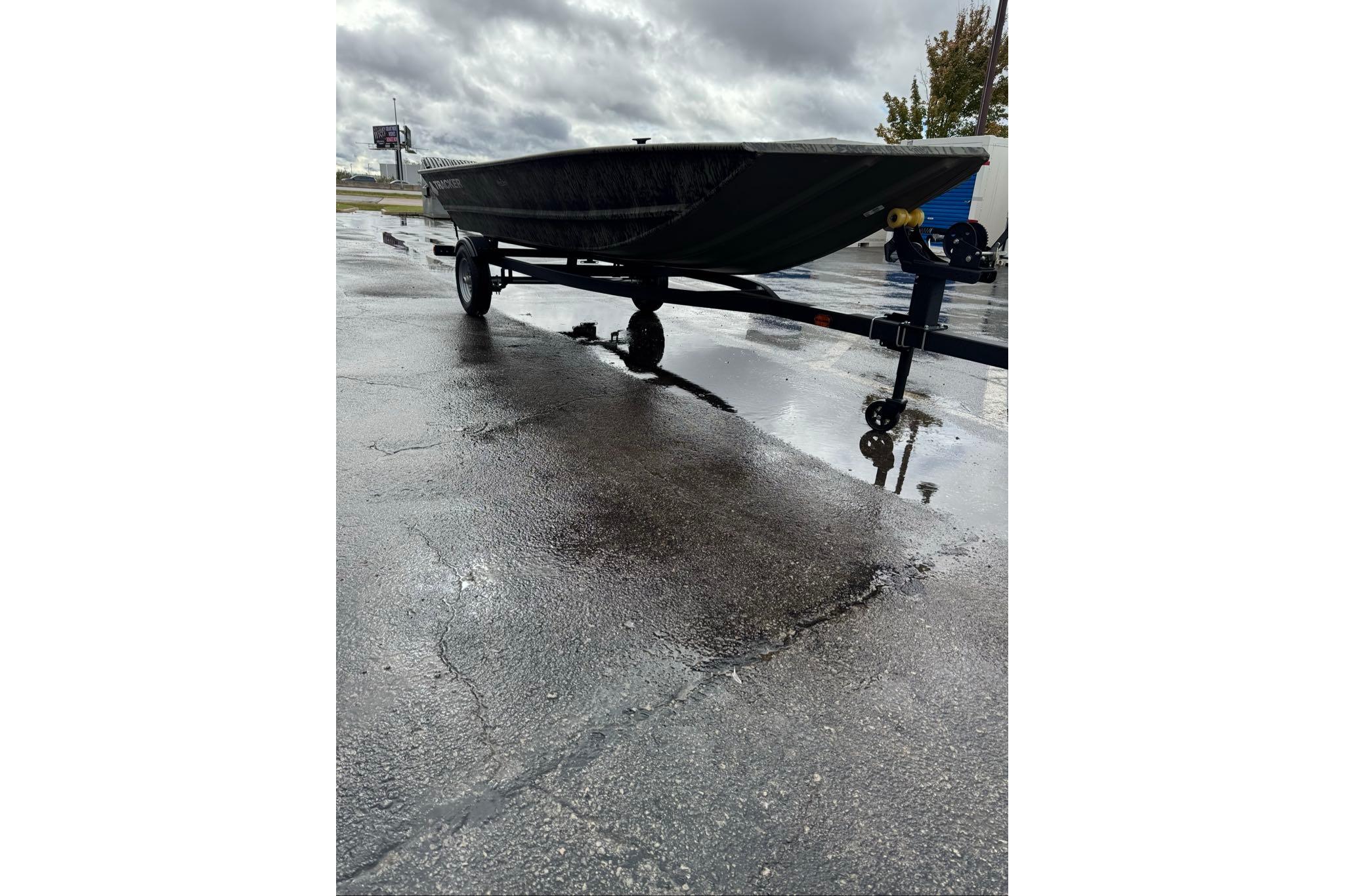 2026 Tracker Grizzly 1648 Utility boat on trailer, parked on wet pavement under cloudy skies.
