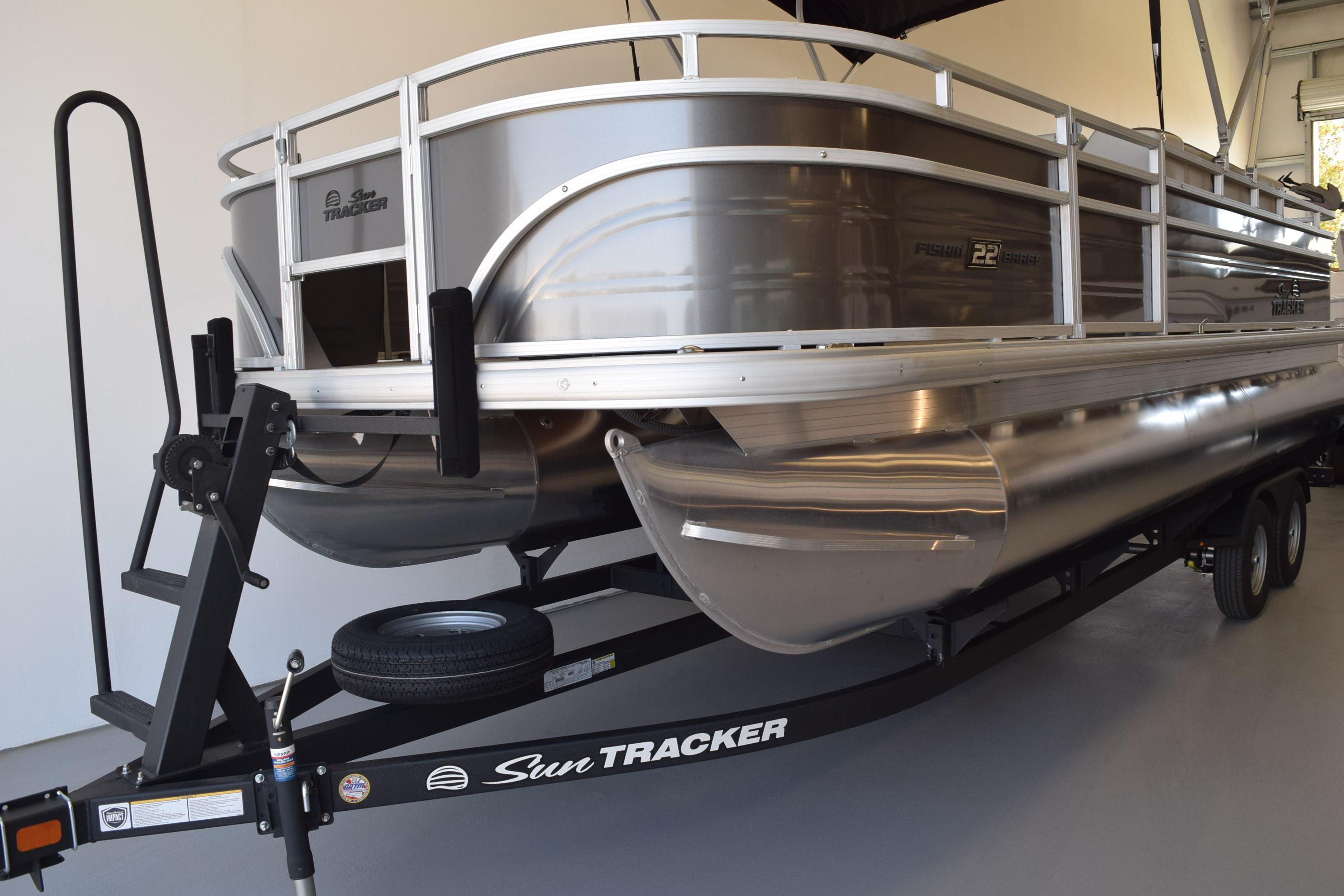 2026 Sun Tracker Fishin' Barge 22 DLX pontoon boat on trailer in showroom.