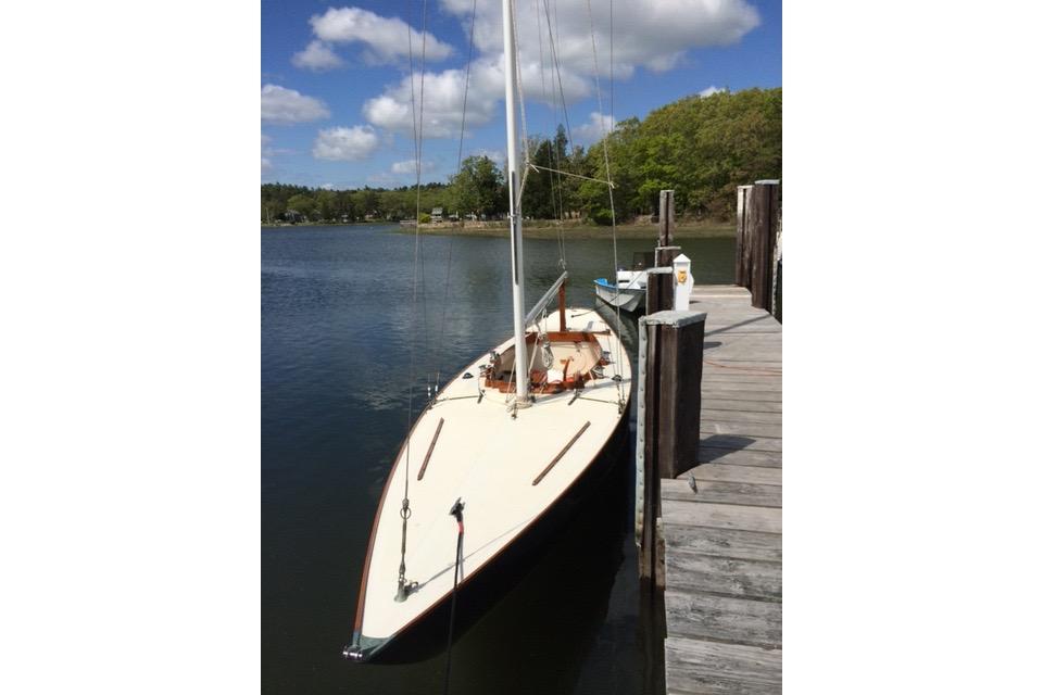 1963 Cape Cod Shipbuilding Shields sailboat docked on a serene lake under a blue sky.