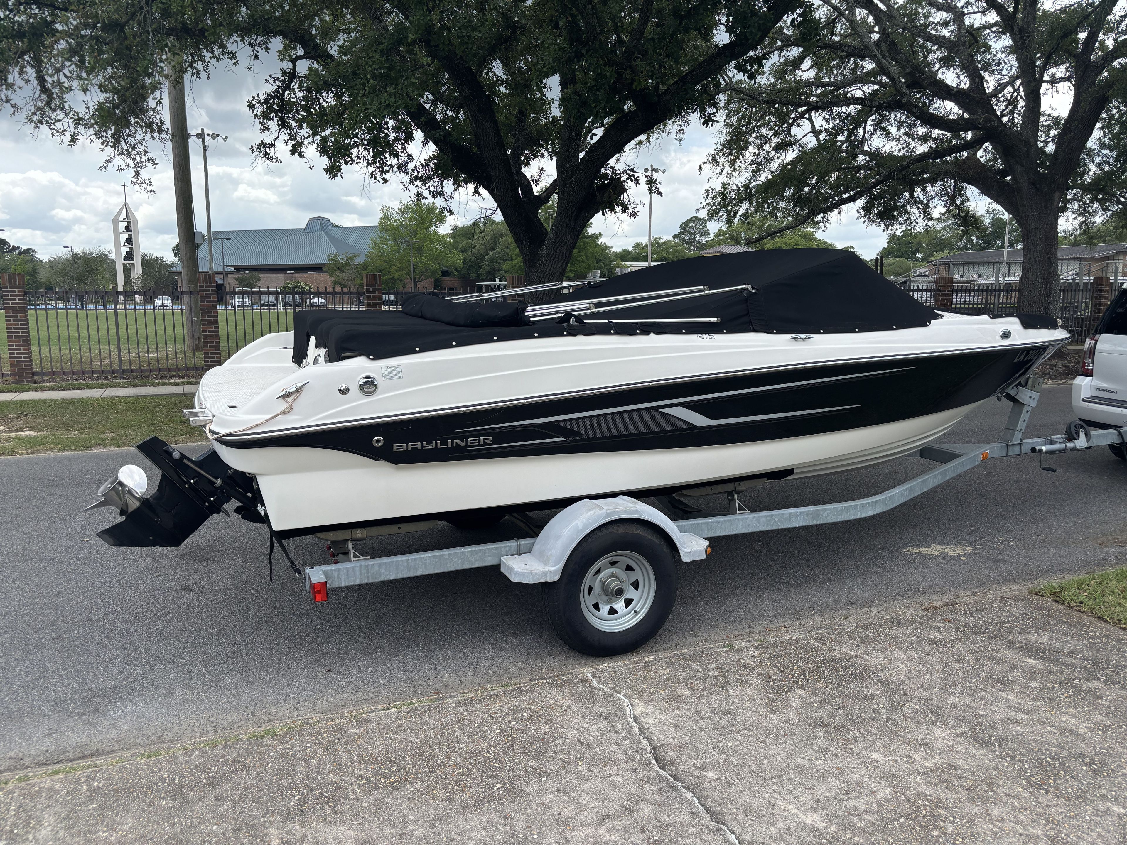 A Bayliner 215 Bowrider boat on a trailer, parked on a street.
