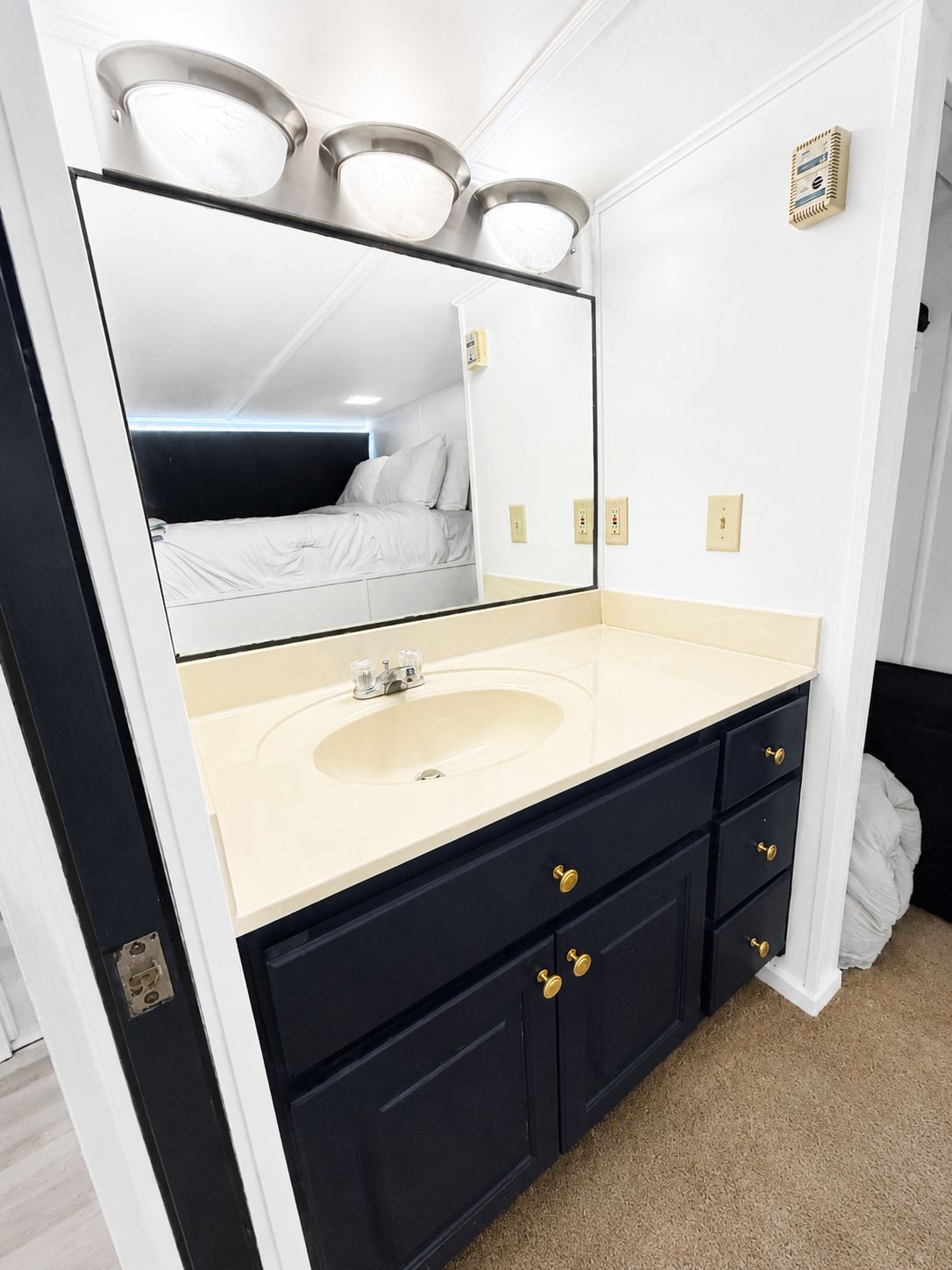 A bathroom with a large mirror, sink, and dark cabinets with gold handles.