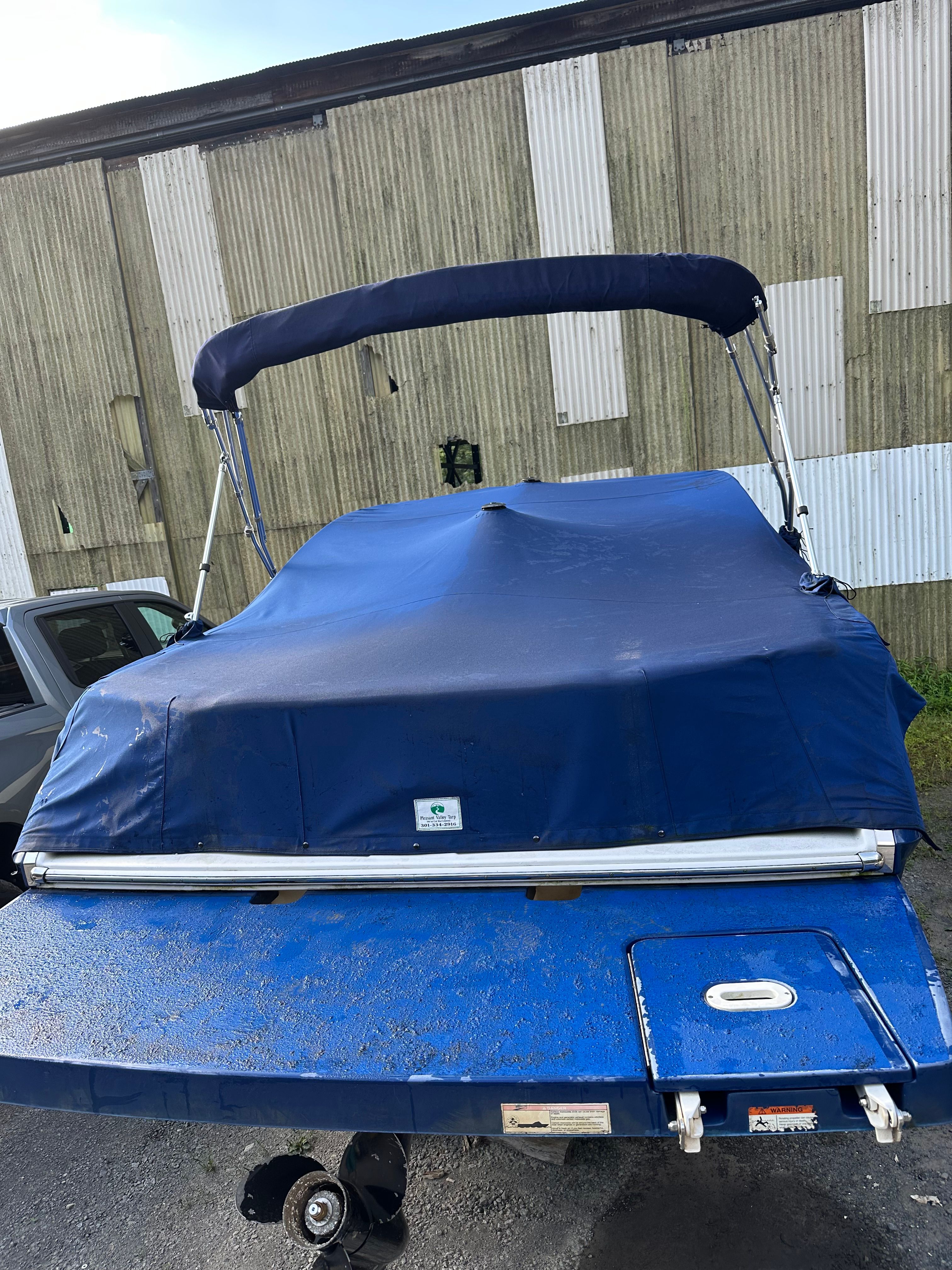 2012 Four Winns H210 boat with blue cover, parked near a building.