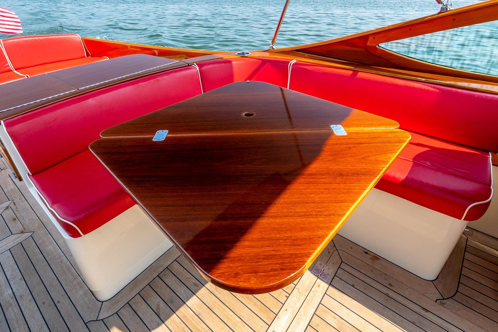 Luxury seating area on 2005 Hinckley Talaria 29R boat with red cushions and wooden table.