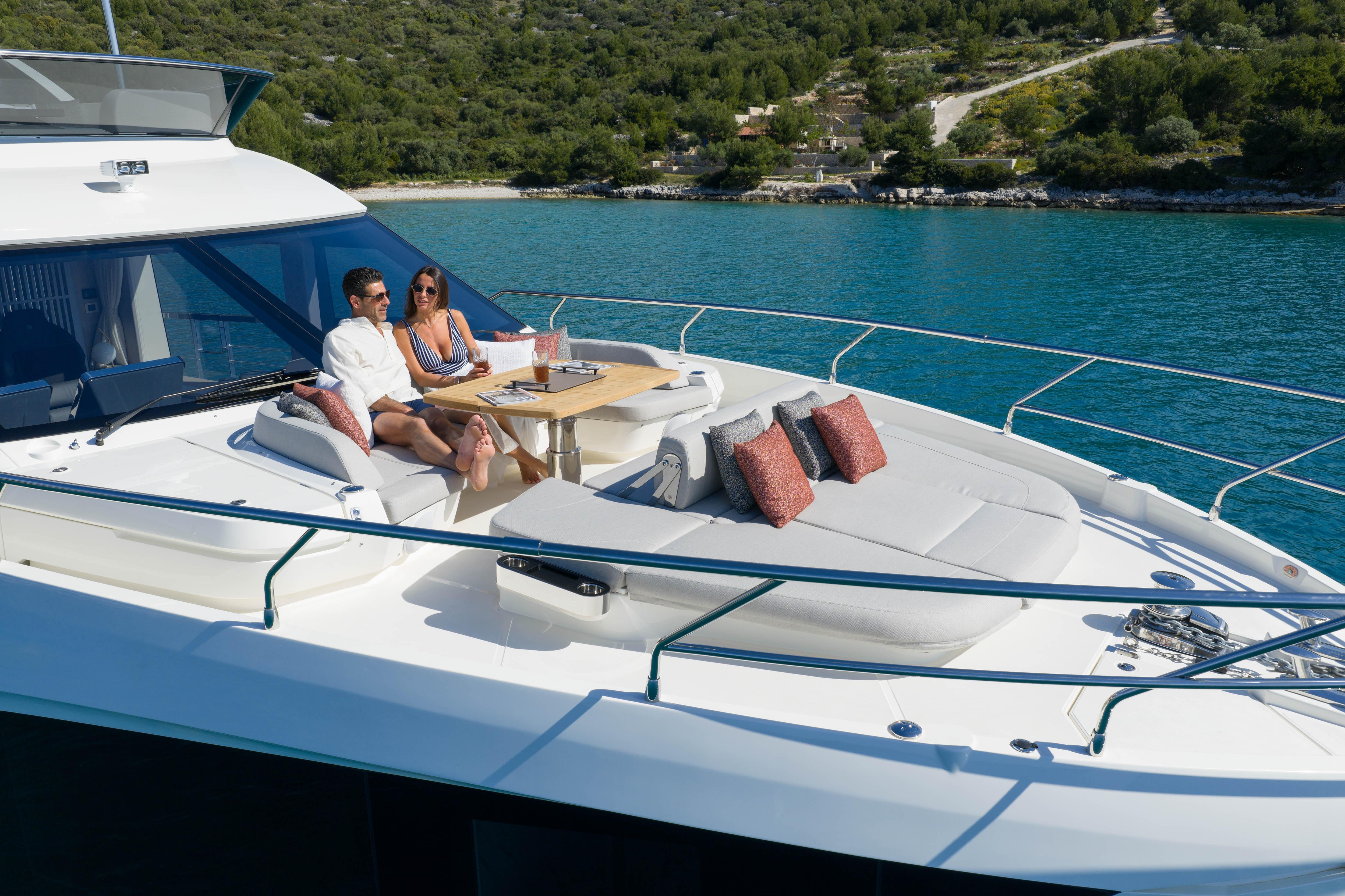 Couple relaxing on a luxurious yacht with cushions and table, surrounded by clear water.