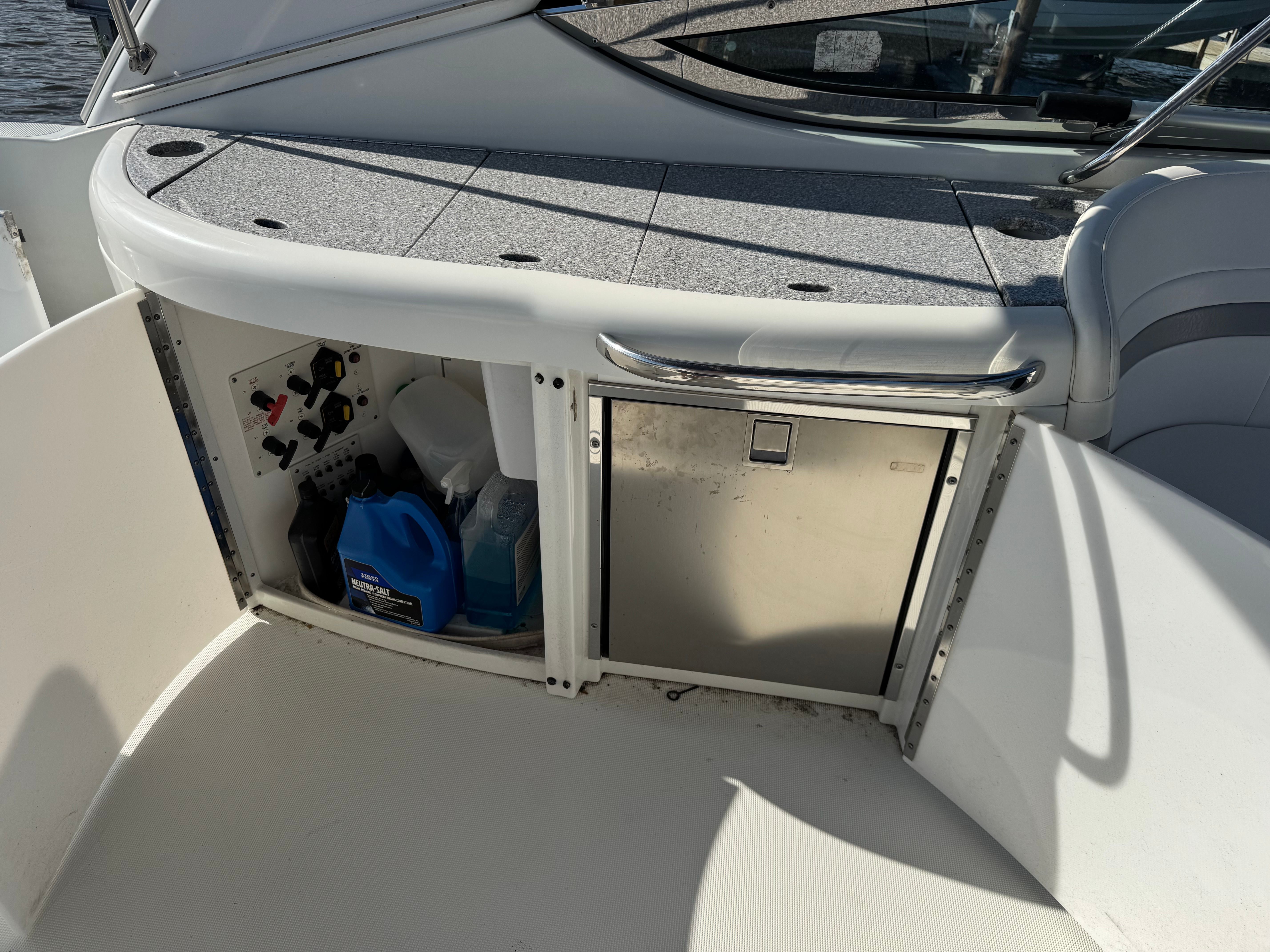 Open storage area on a boat with cleaning supplies and a refrigerator.