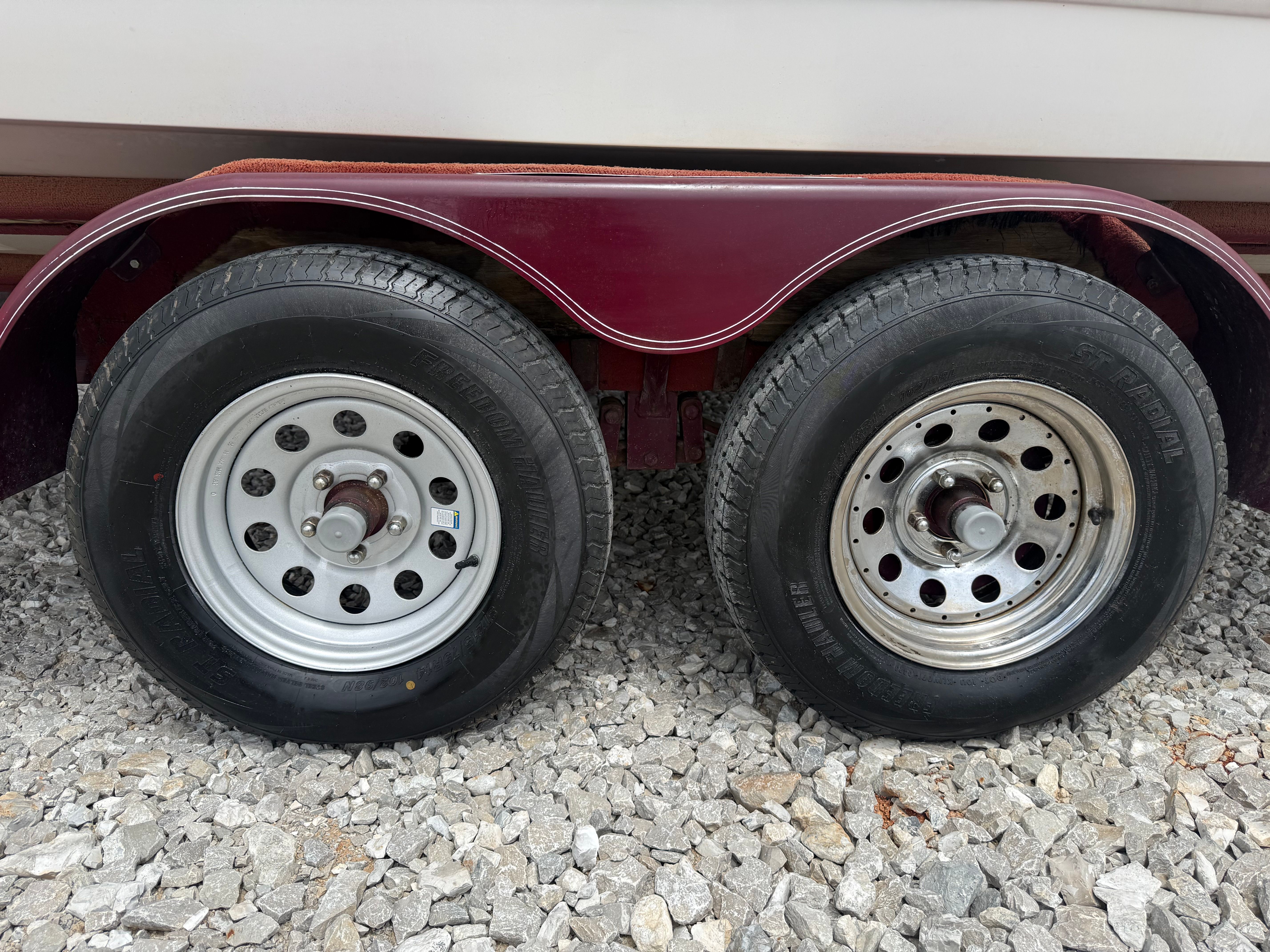 Close-up of two tires on a trailer with a gravel surface.