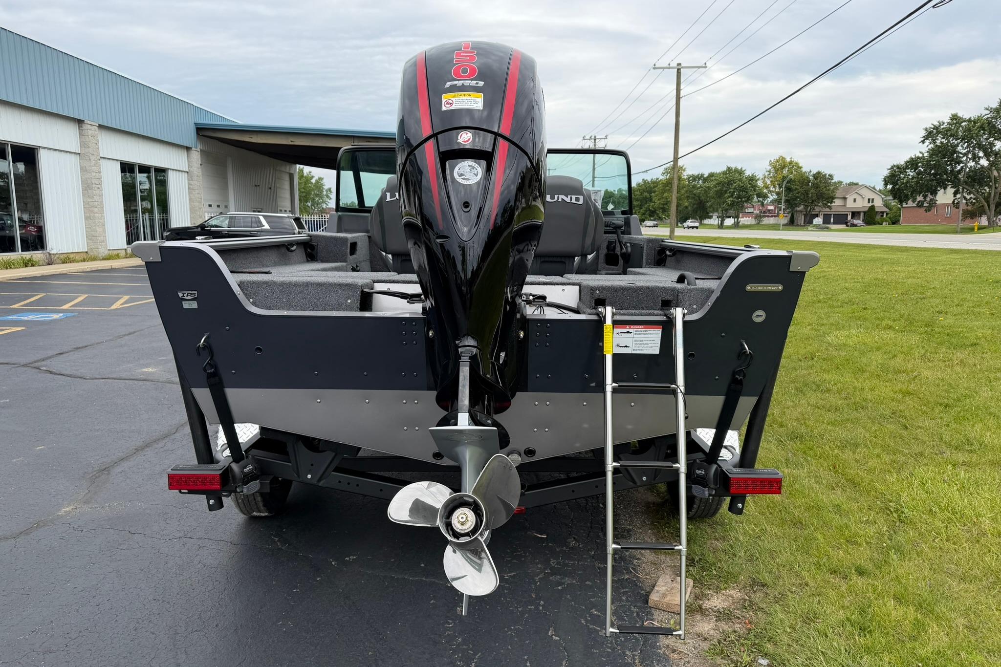 2027 Lund 1875 Impact XS Sport boat with outboard motor and ladder, parked outdoors.