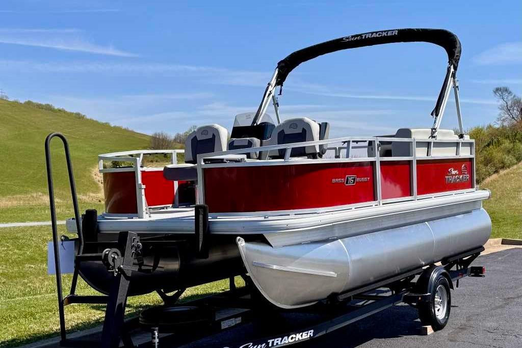 2026 Sun Tracker Bass Buggy 16 XL Select pontoon boat on trailer, parked outdoors.