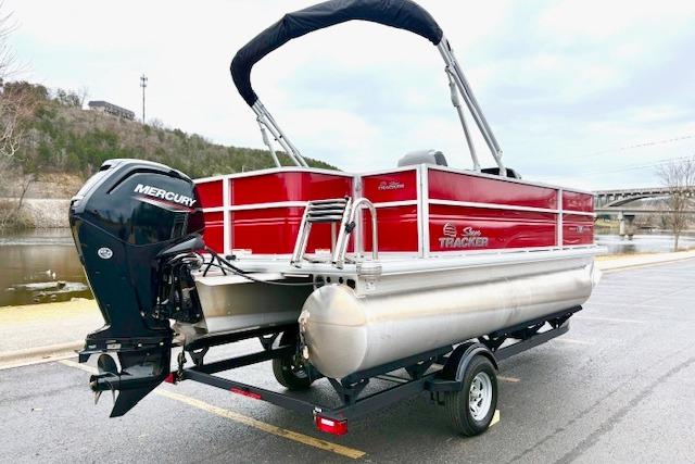 2026 Sun Tracker Party Barge 18 DLX pontoon boat with Mercury engine, parked near a river.