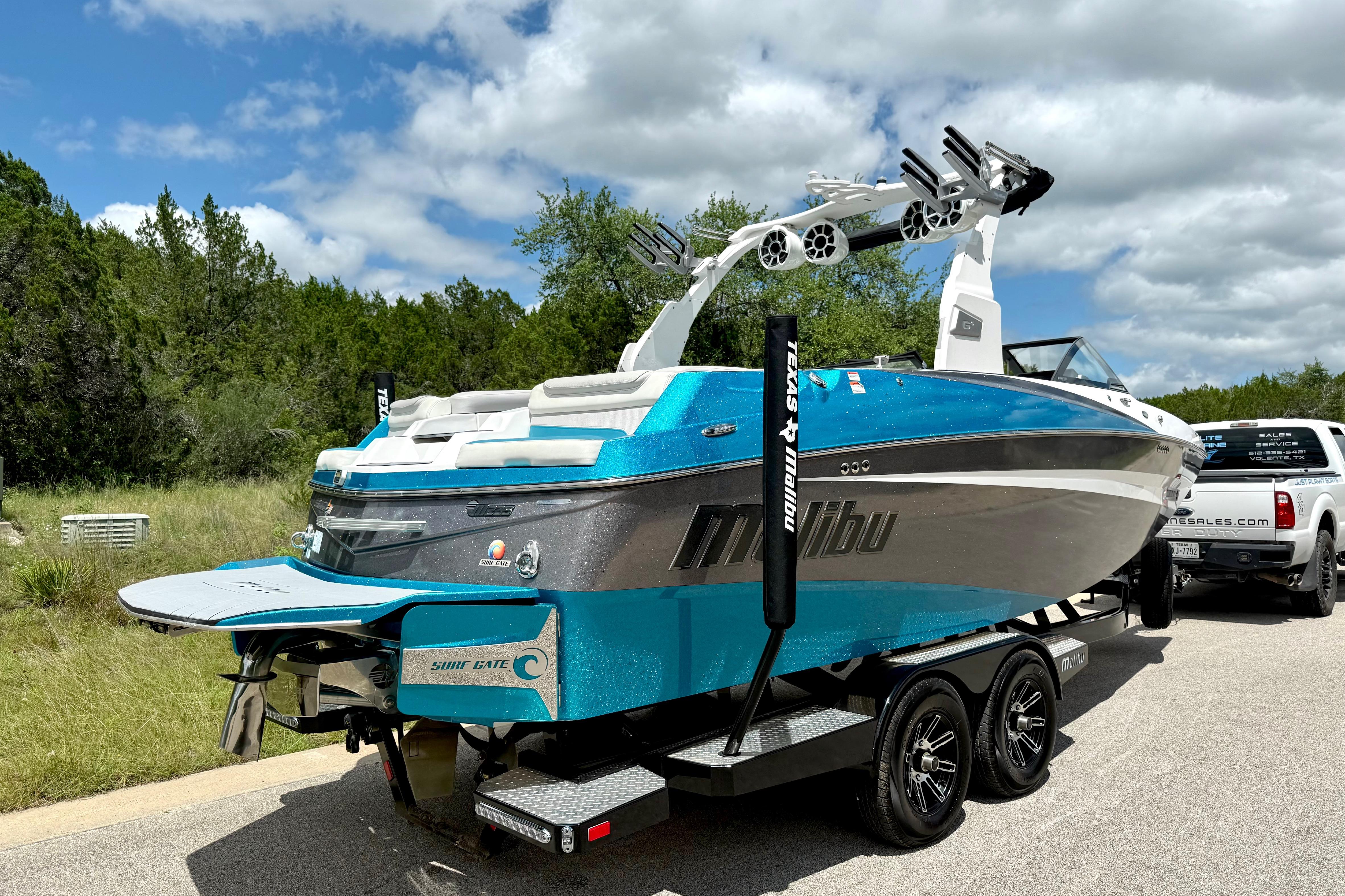 2017 Malibu M235 boat on trailer, vibrant blue and silver, parked outdoors under cloudy sky.