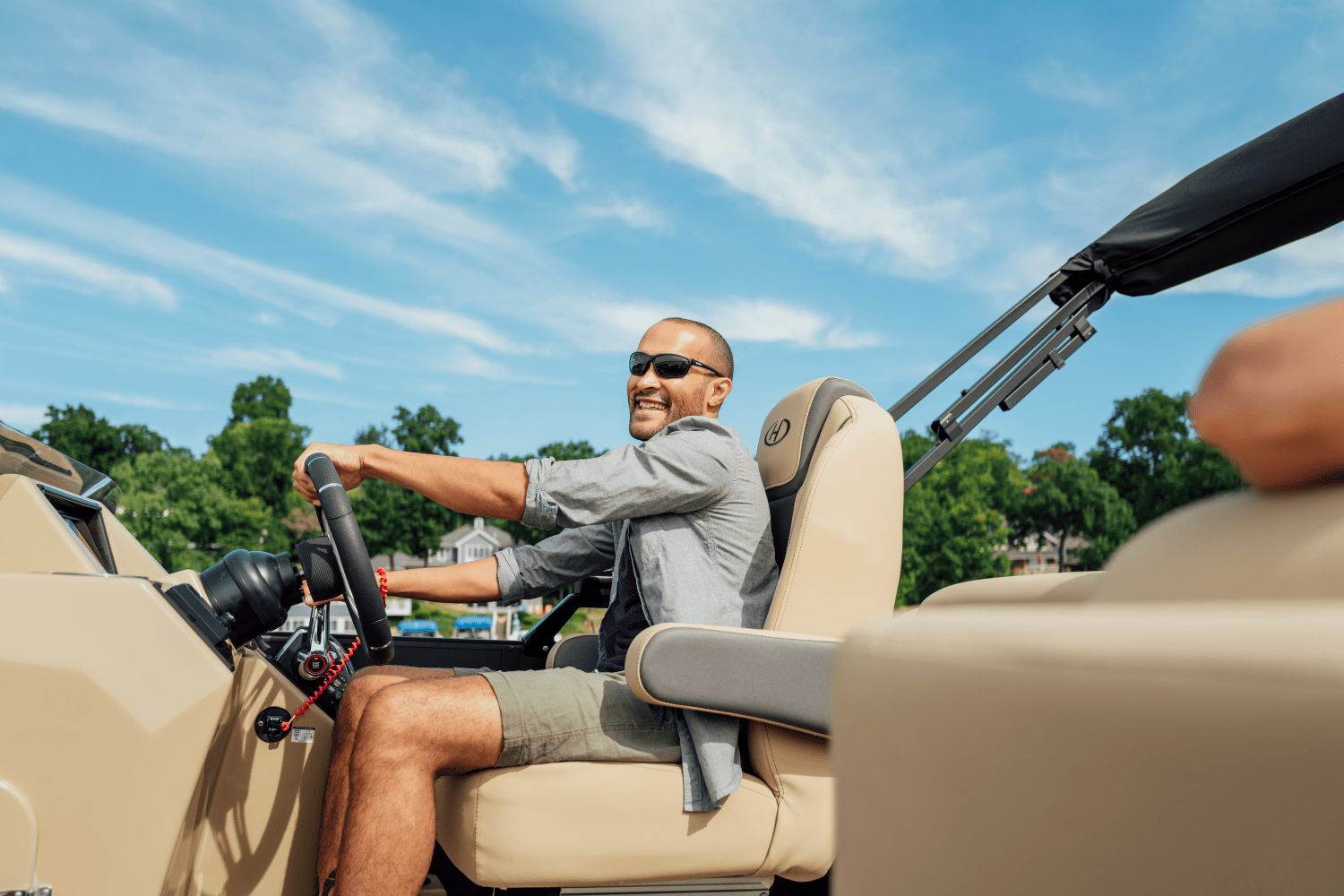 A man is steering a Harris Cruiser 230 boat on sunny waters.