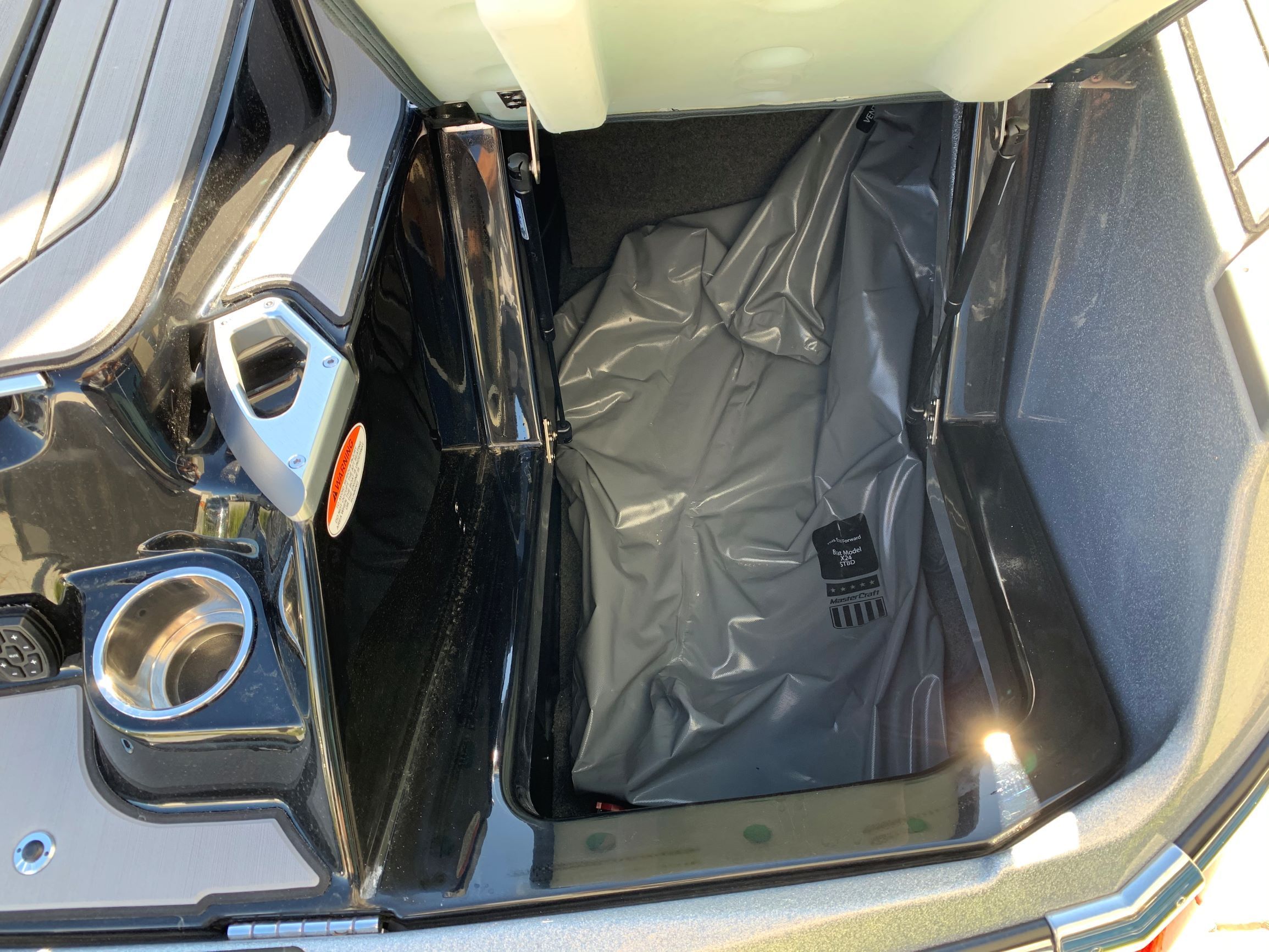 A storage compartment in the rear of a MasterCraft X24 boat with a gray cover.