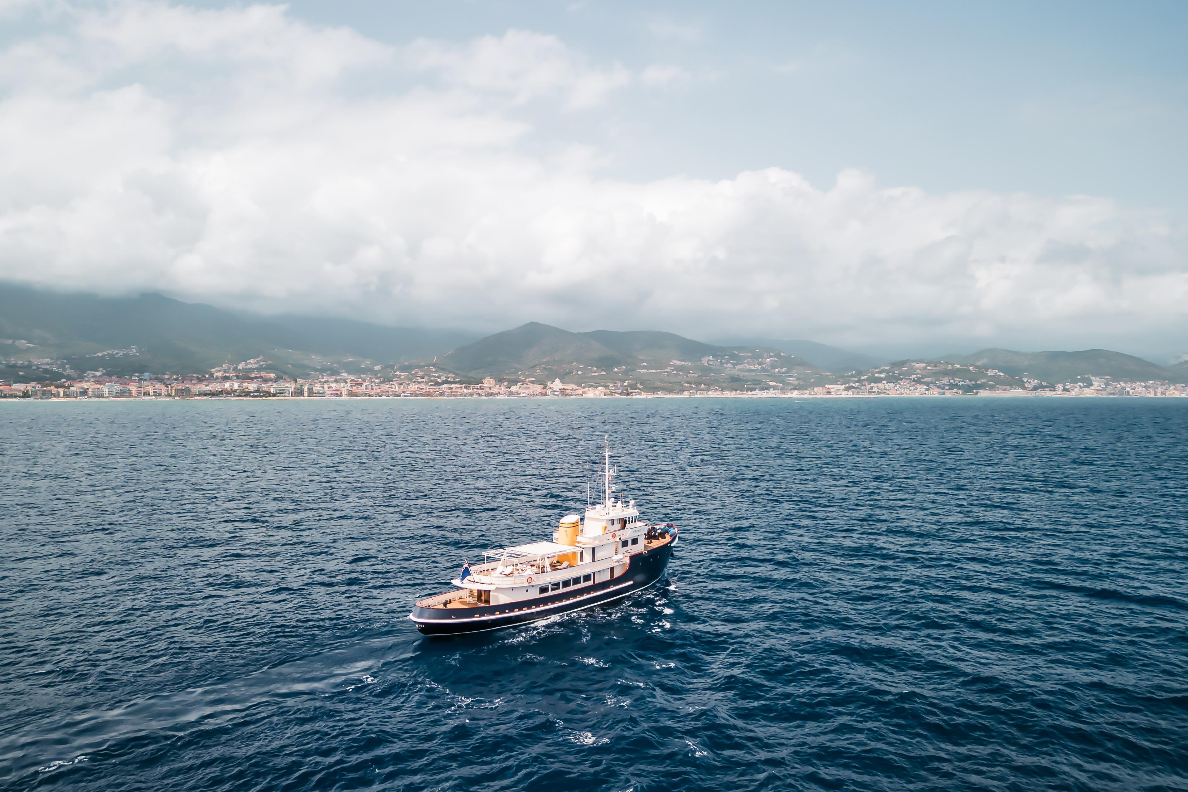 Vintage 1956 custom converted tugboat cruising on open sea with coastal town backdrop.