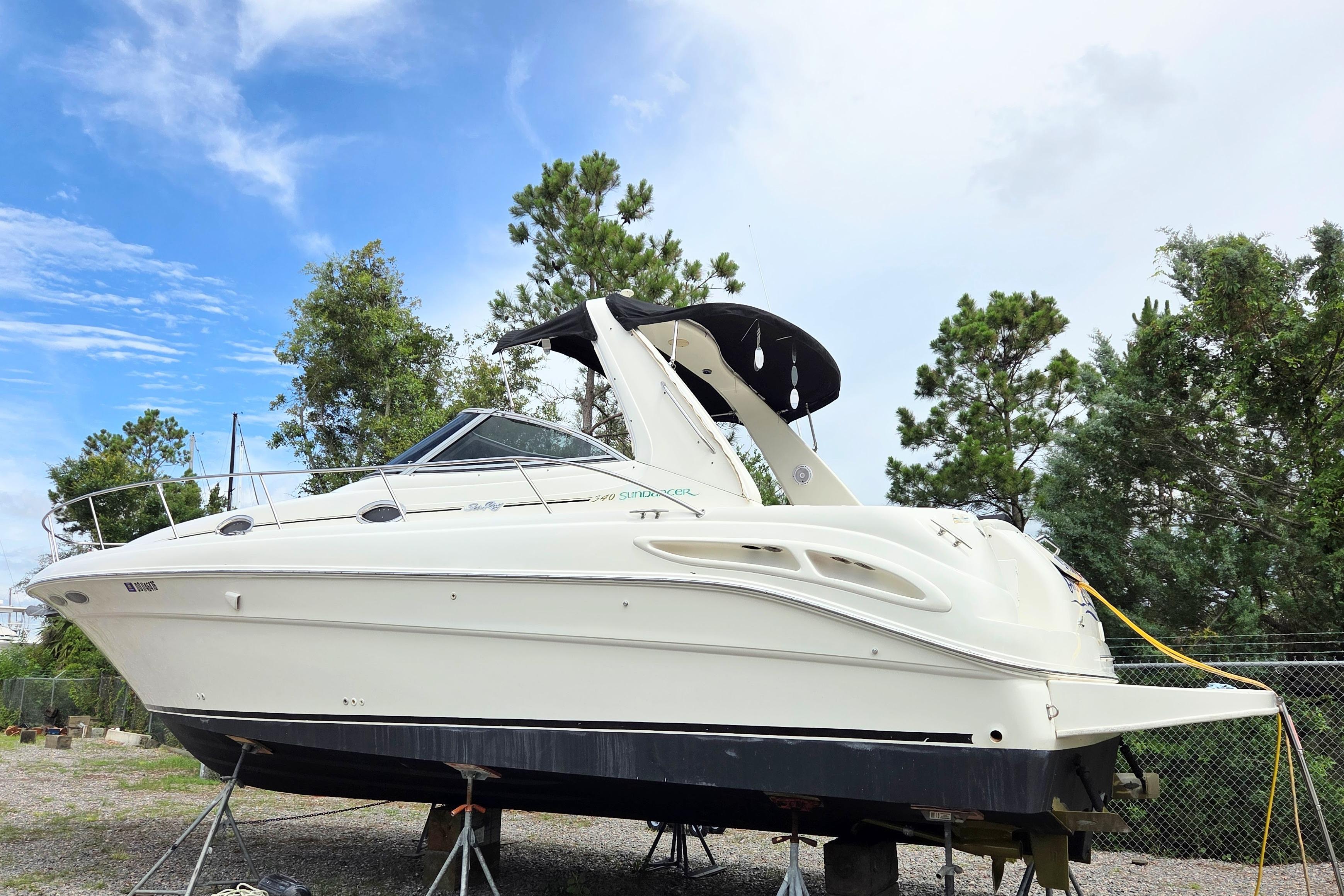 2000 Sea Ray 340 Sundancer boat on stands, surrounded by trees and a clear sky.