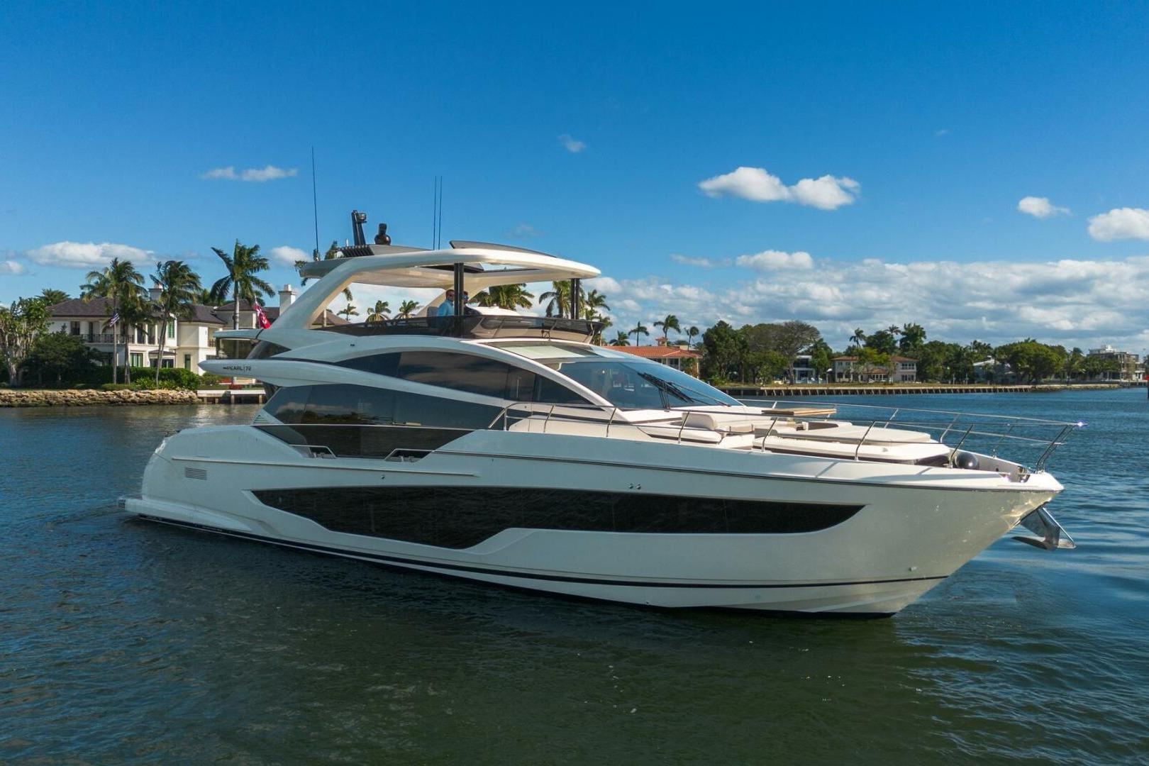 Luxurious 2023 Pearl 72 yacht cruising on a sunny day near waterfront homes.